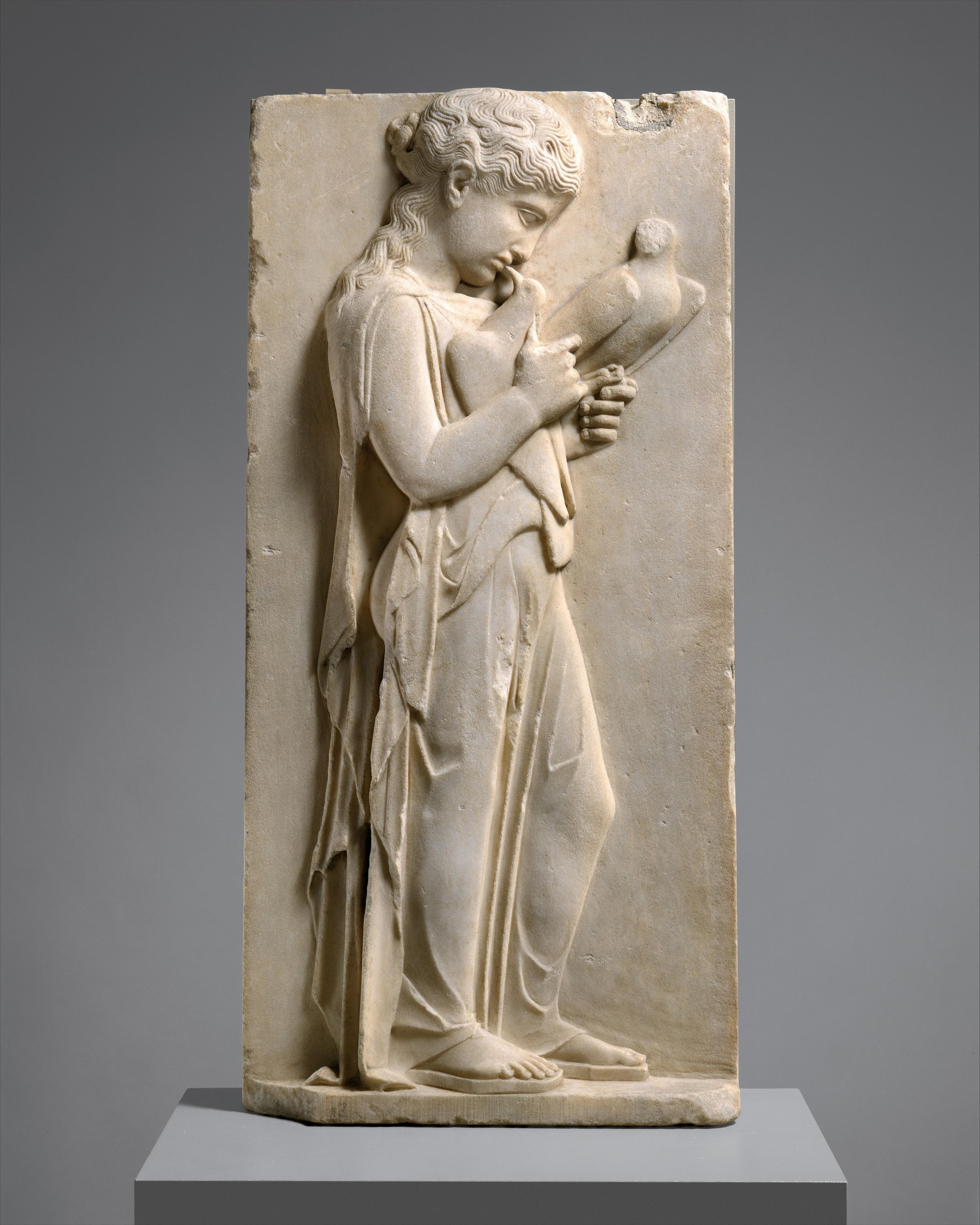 Marble grave stele carved with a young girl holding two doves.