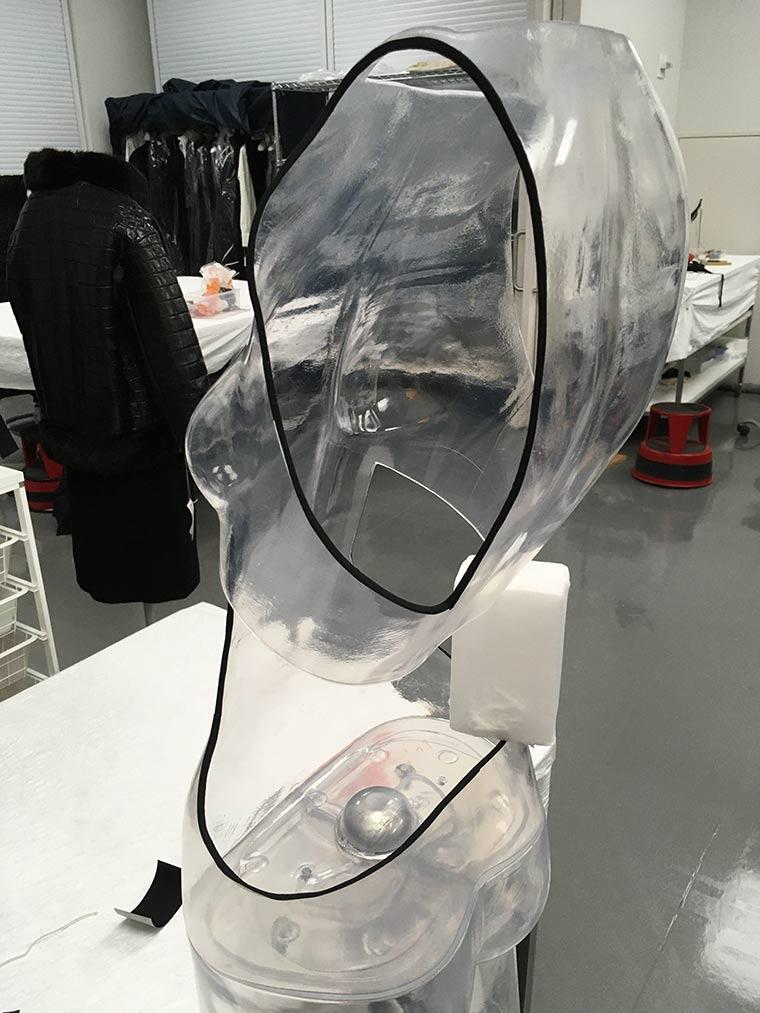 Back of a clear dress mount in the shape of a mannequin with large cutouts for each arm and the lower back