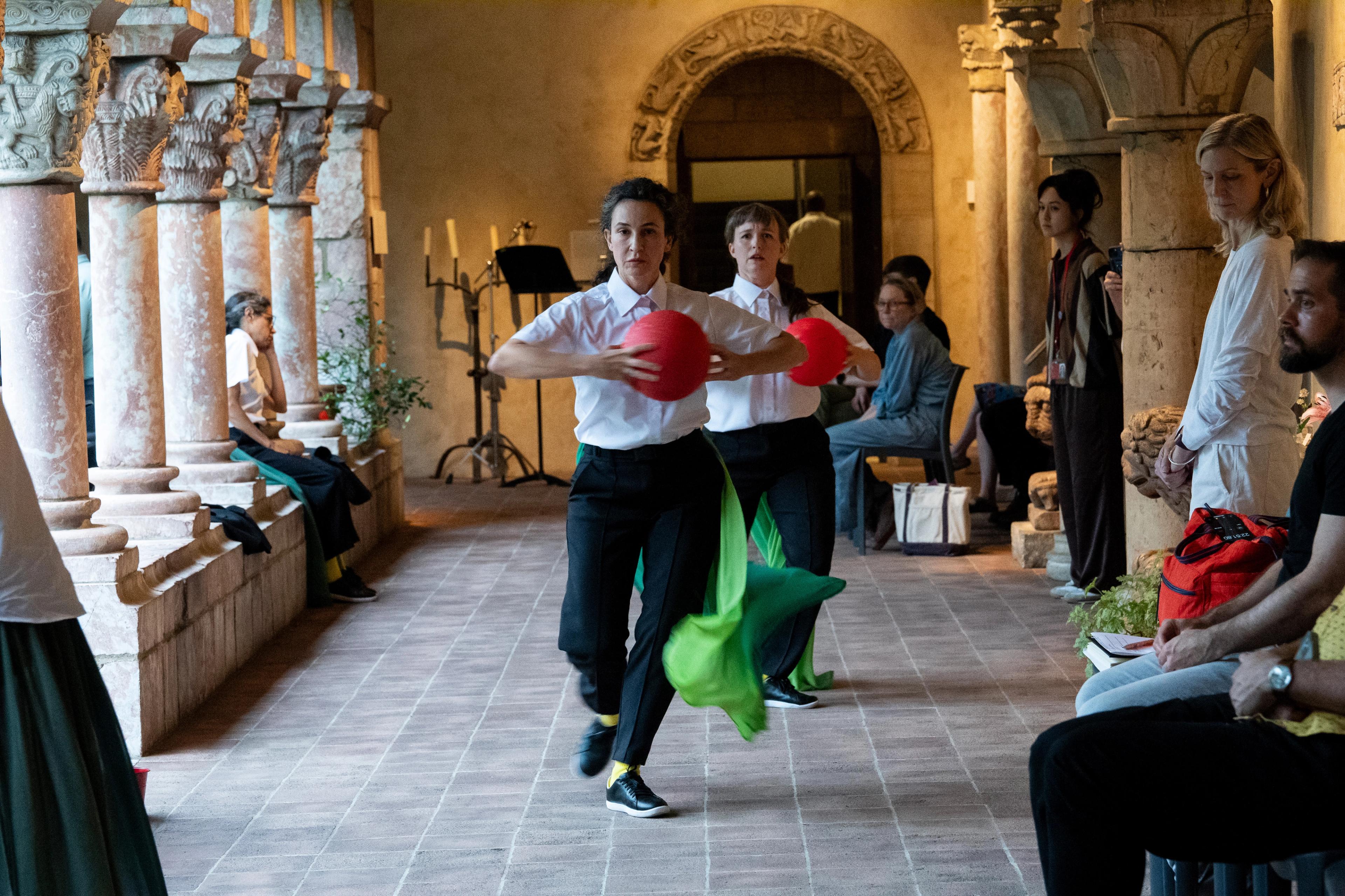 A parade of actors holding red balls, with a train of green fabric flapping at their legs.