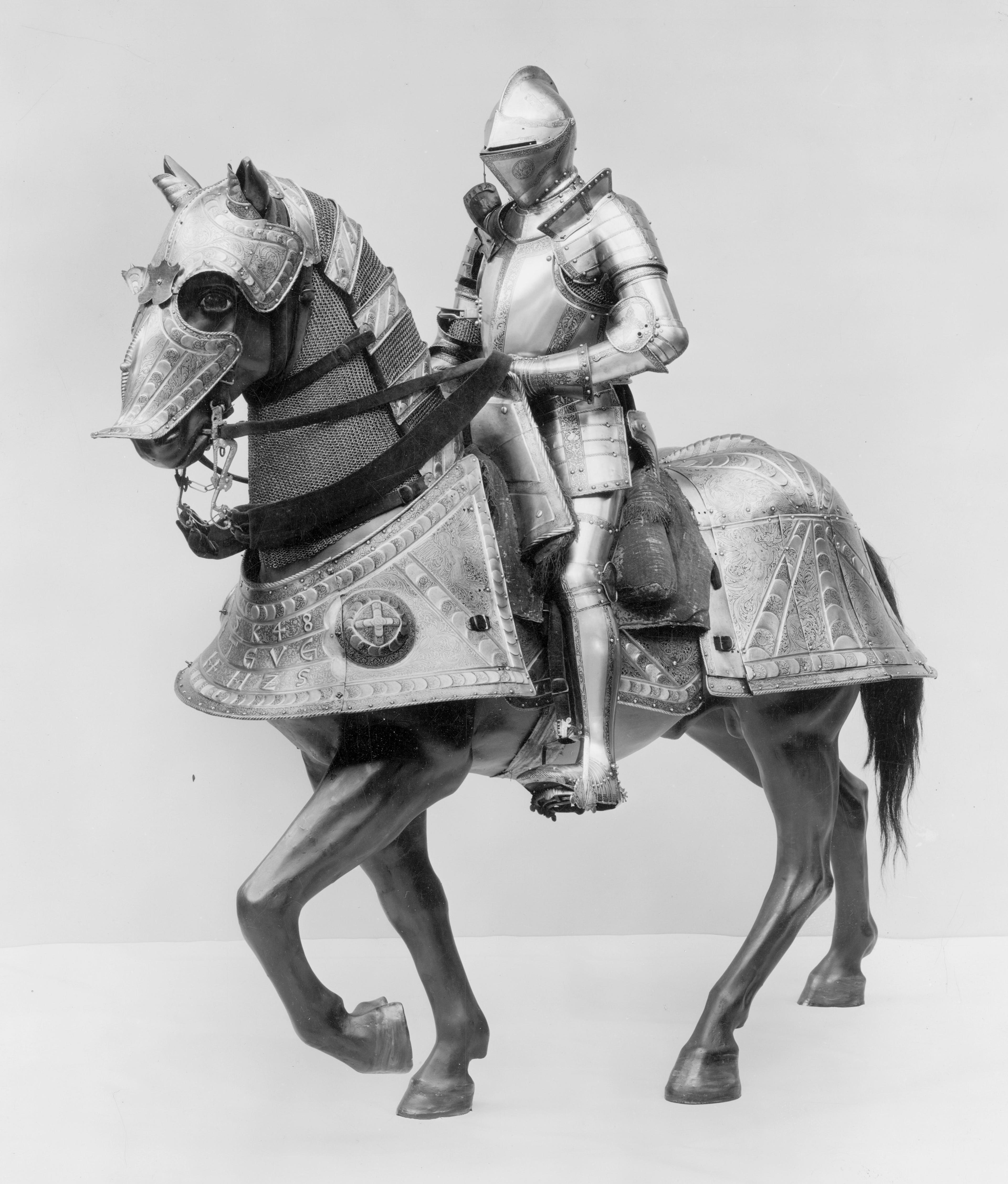 Black and white photograph of a man in a full suit of armor riding a horse also wearing armor.