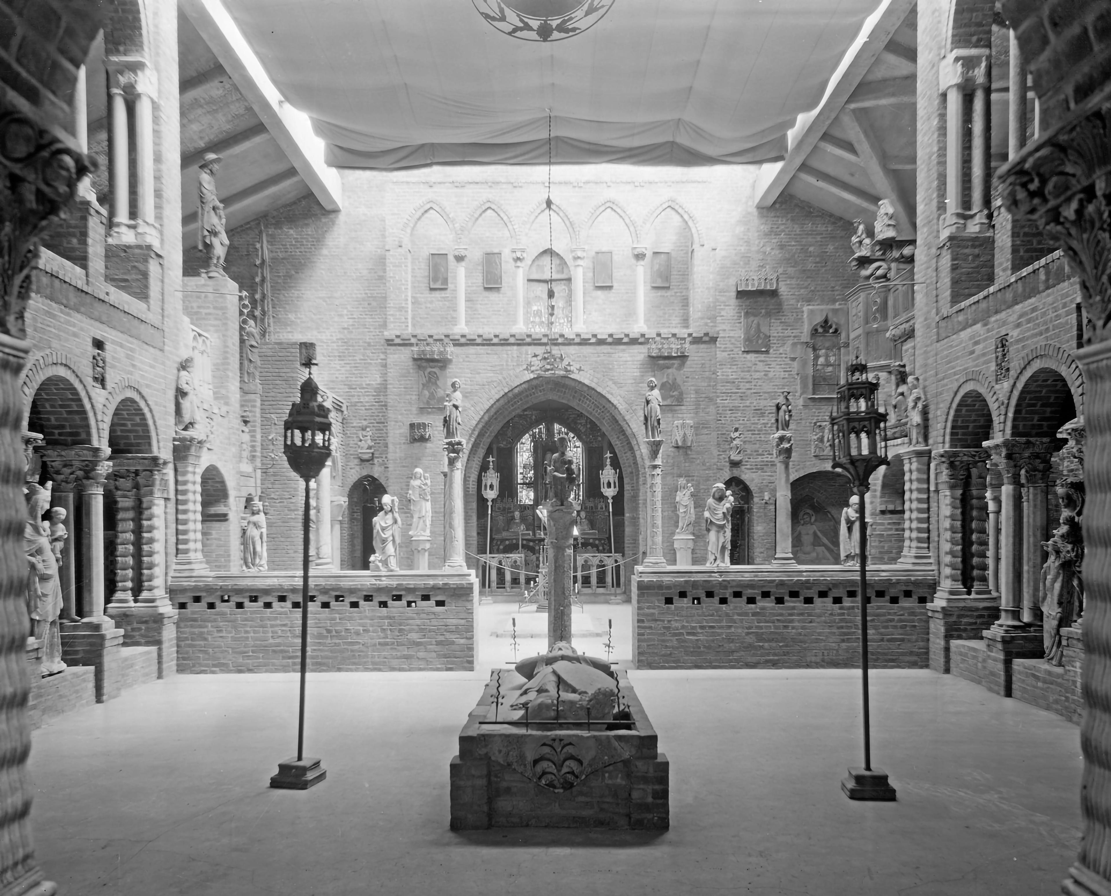 Medieval-style hall with brick arches and statues, illuminated by lanterns arranged around a central stone structure.