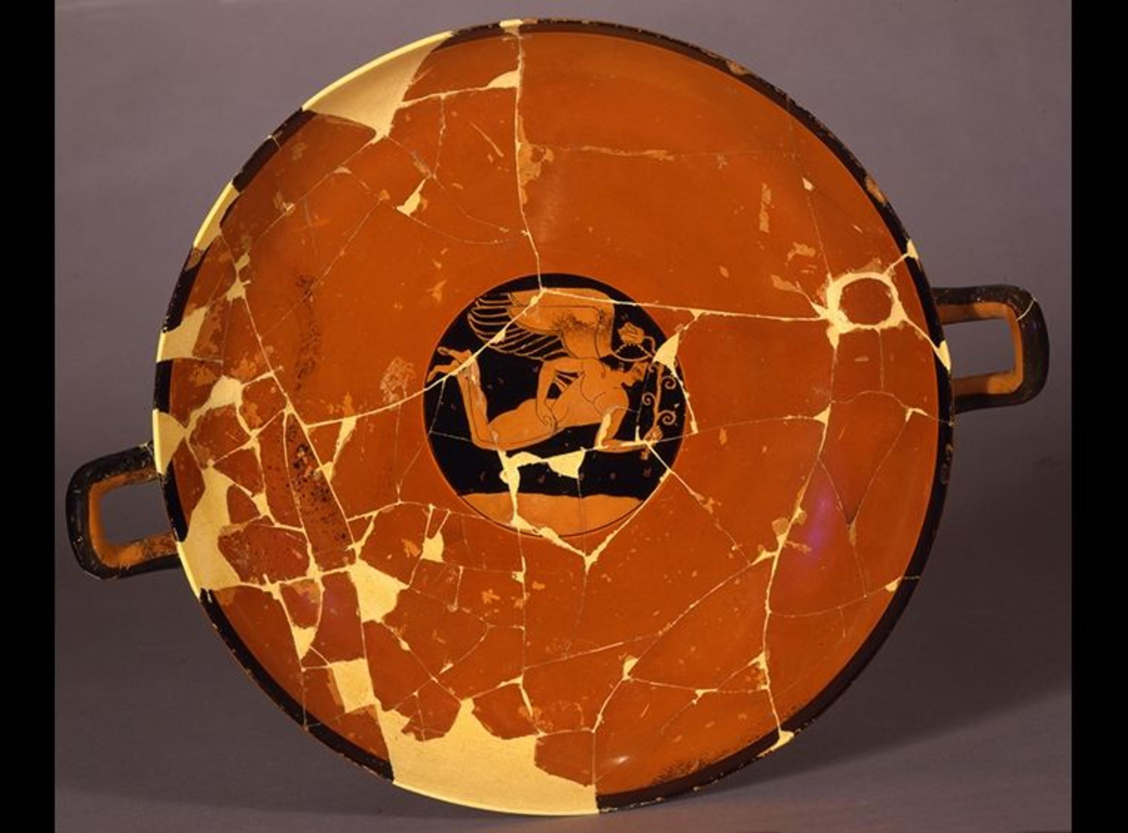A red Greek drinking cup with a painting of a winged figure in flight holding a flower