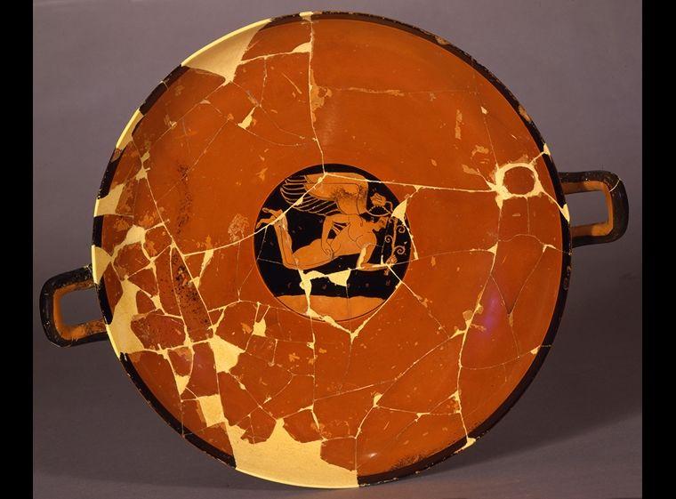 A red Greek drinking cup with a painting of a winged figure in flight holding a flower