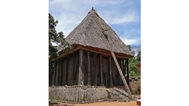 A building of a shrine, with a ladder leaned against it and a figure sitting on top