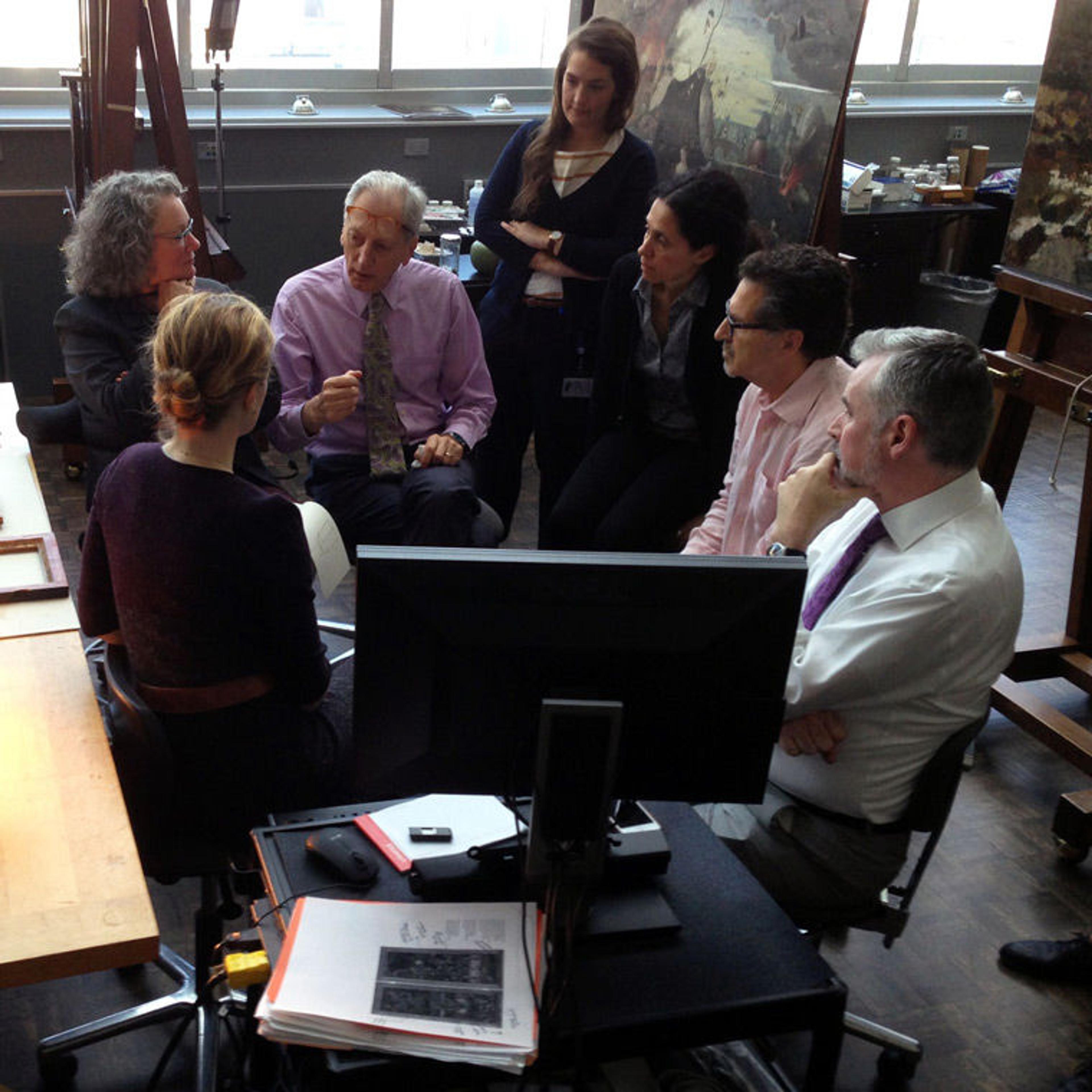 A group of art experts hold a discussion in a brightly lit conservation studio