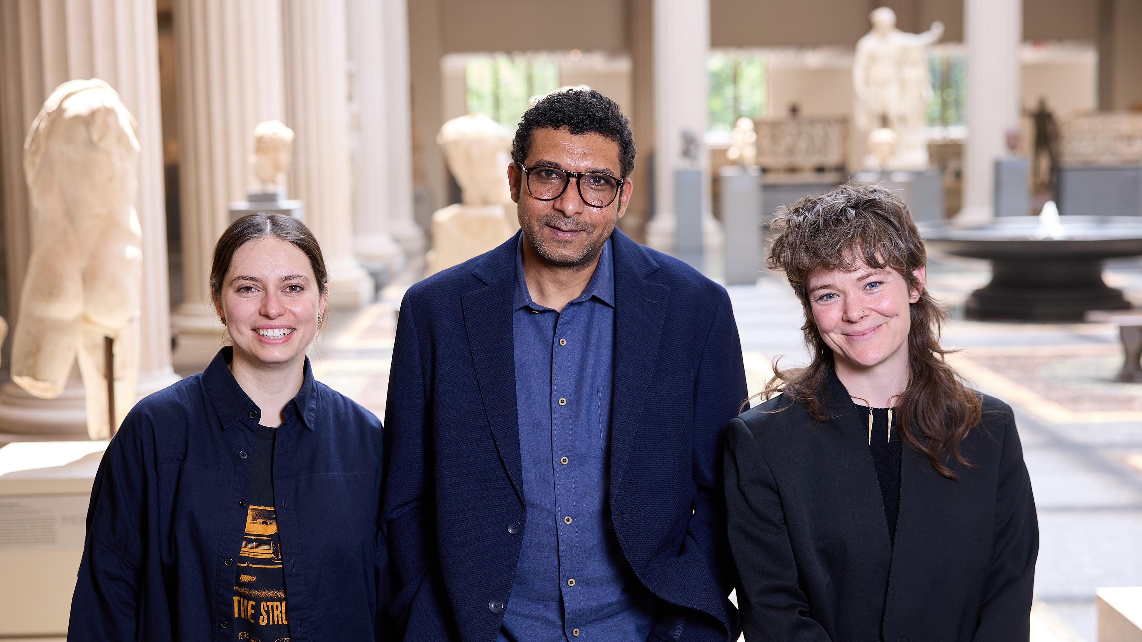 three people standing in greek and roman galleries one is male with glasses