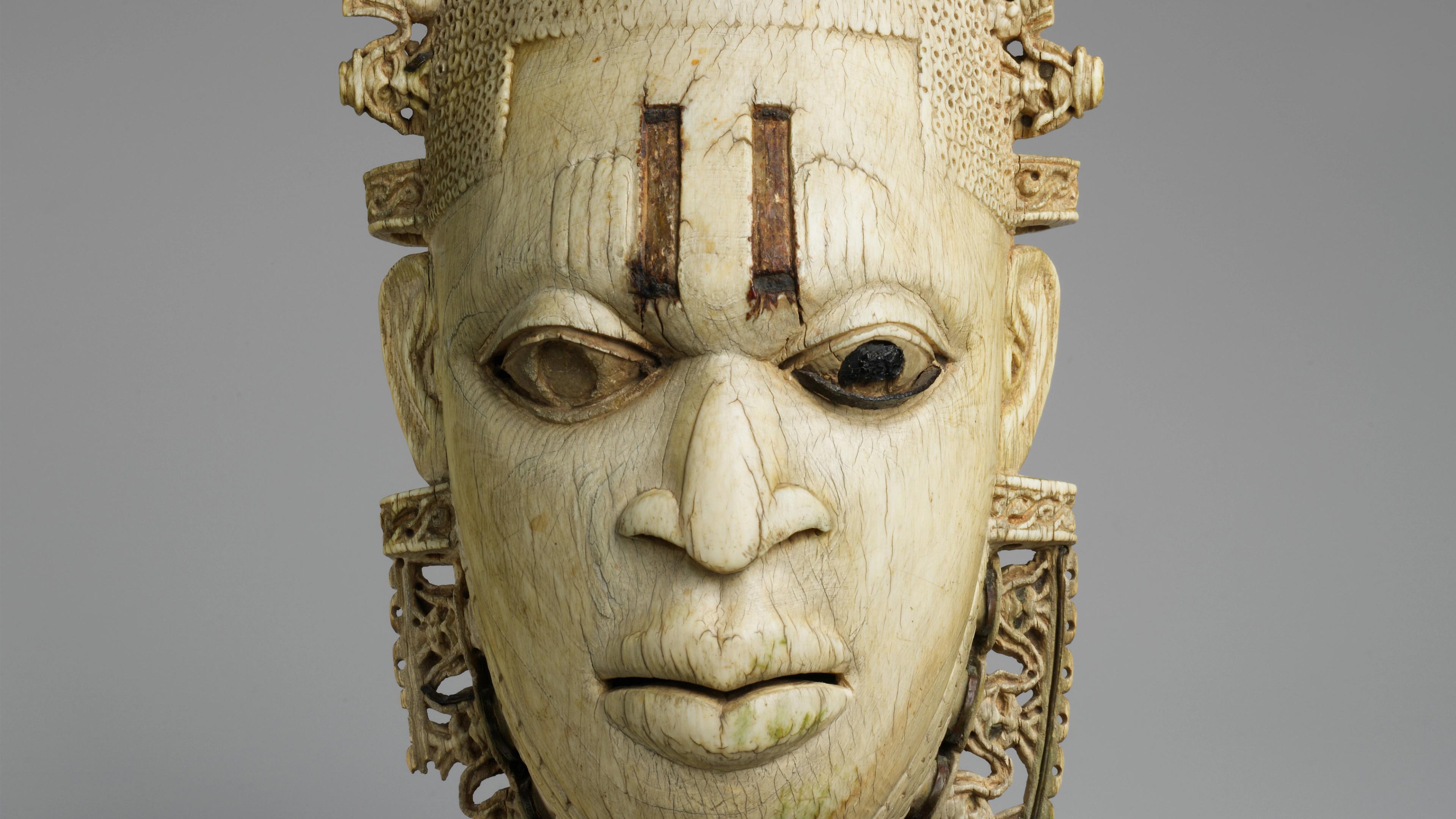 Ivory pendant mask carved in the shape of a woman's face with two vertical lines carved as scarification marks on the forehead
