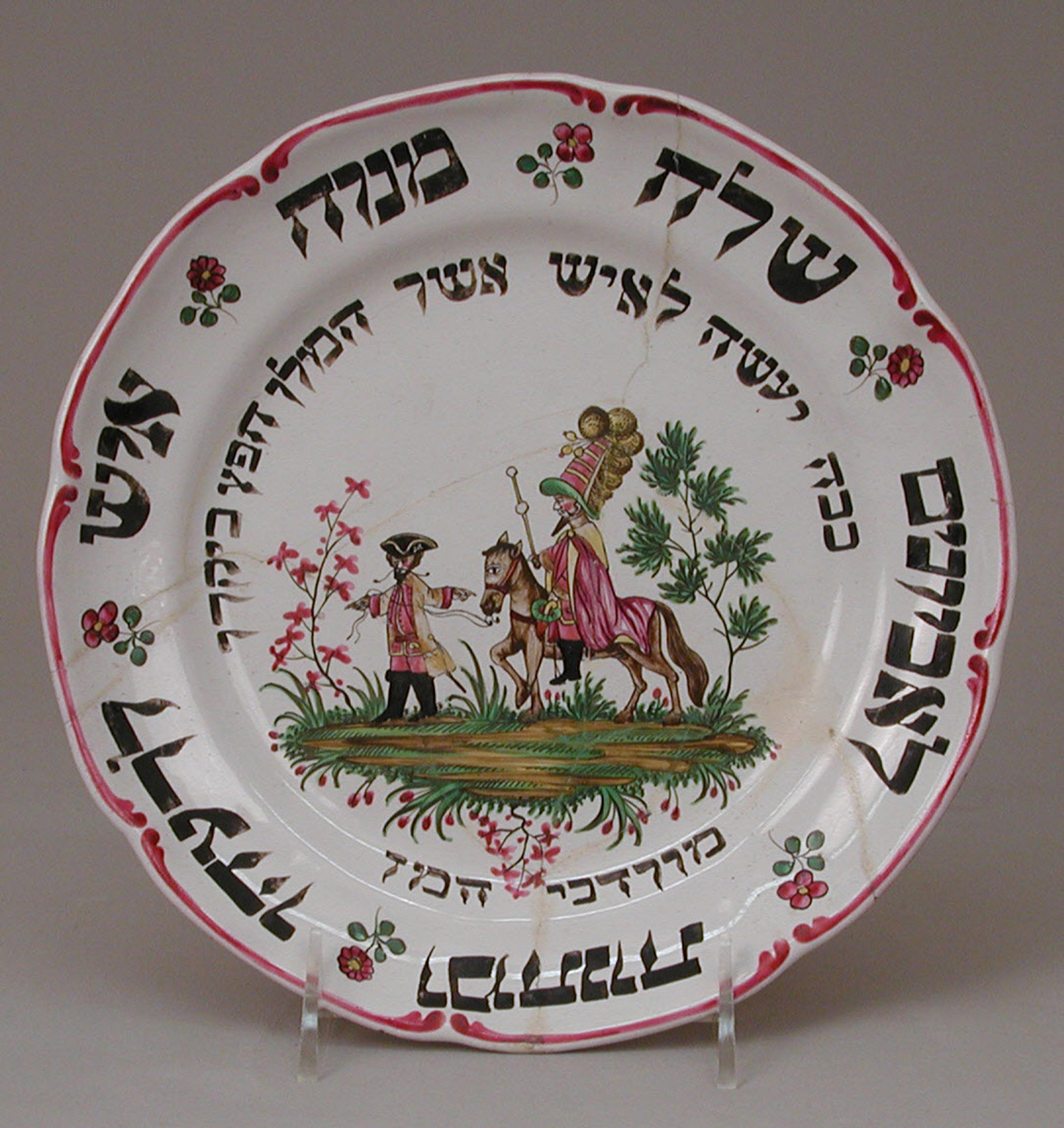 Ornate plate with Hebrew script at center, surrounded by vibrant pink floral patterns and green leaves on a white background.
