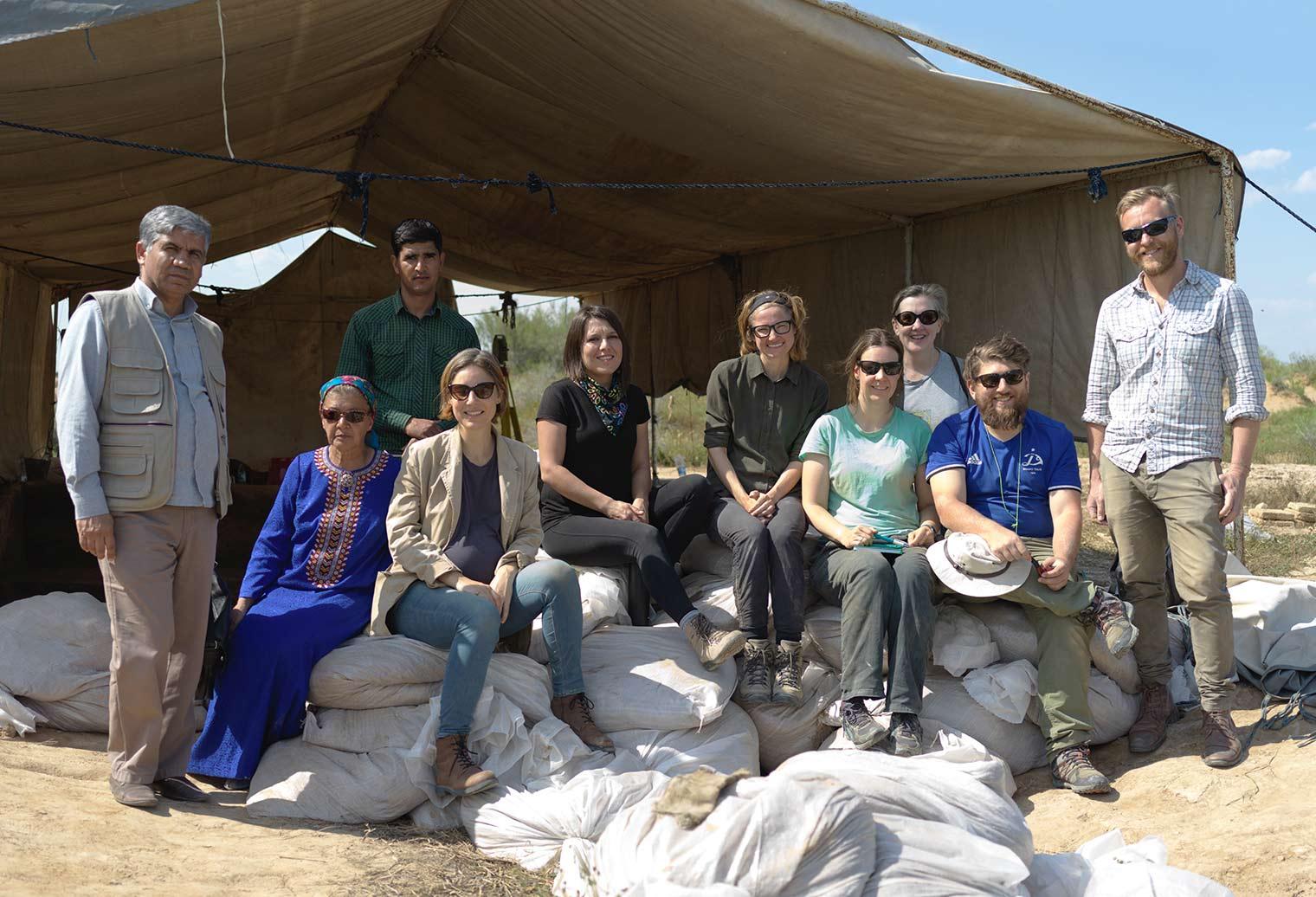 Photograph of a team of archeologists seated outdoors in front of a tent