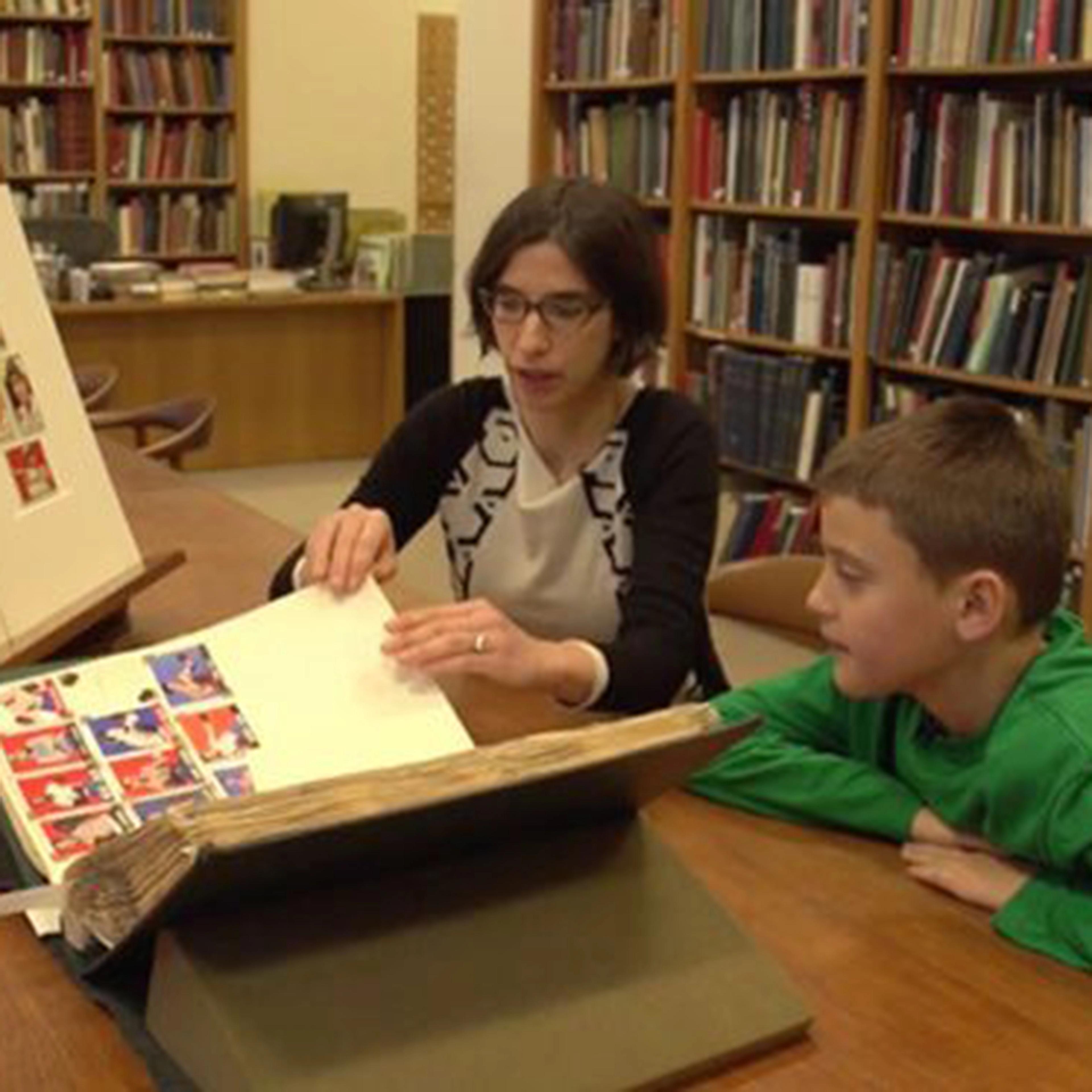 A woman and a child sit at a desk holding displays of sports cards