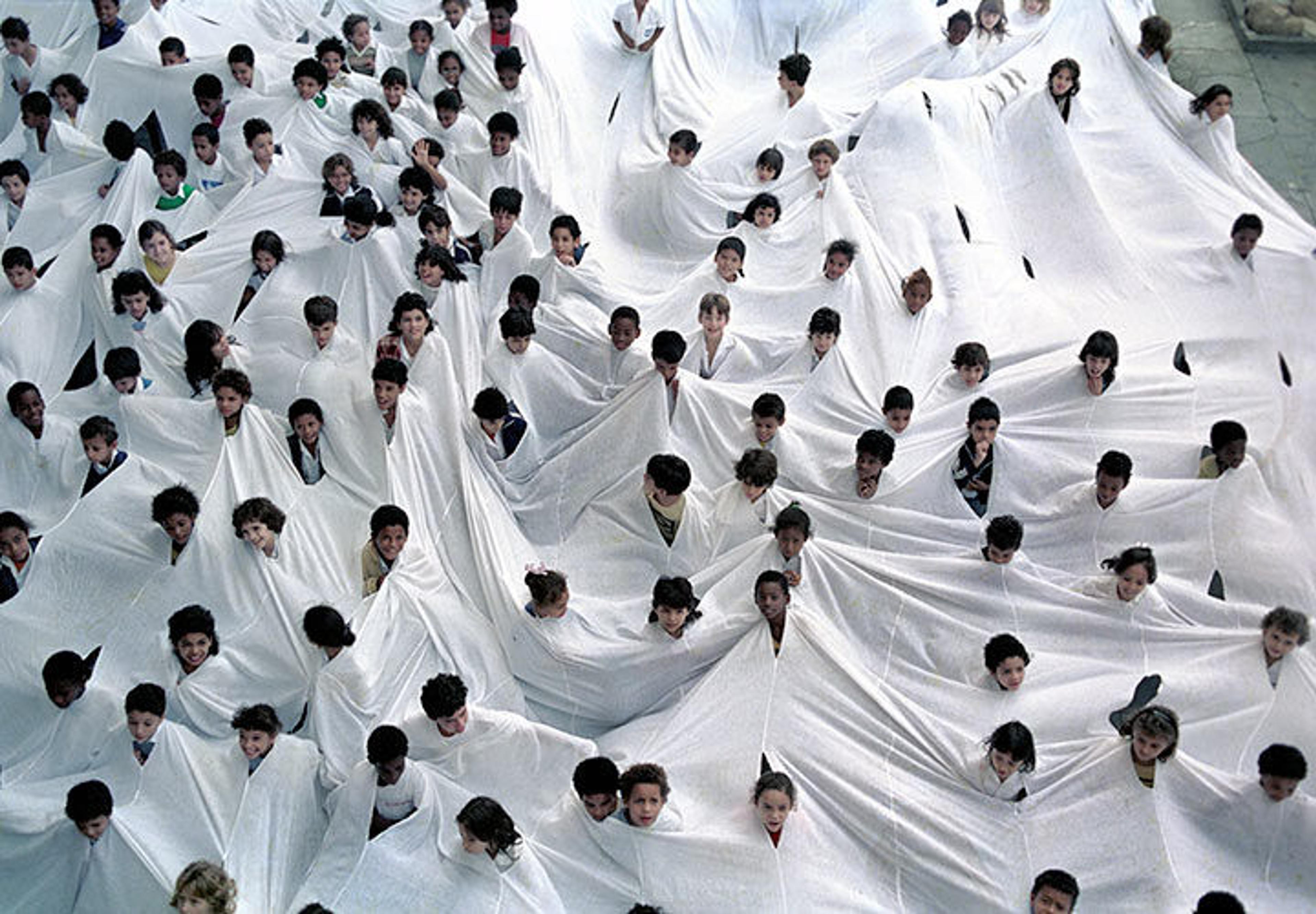 A multitude of people's heads emerging from a huge piece of white fabric