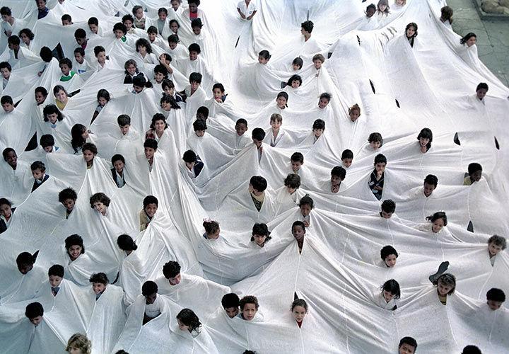 A multitude of people's heads emerging from a huge piece of white fabric