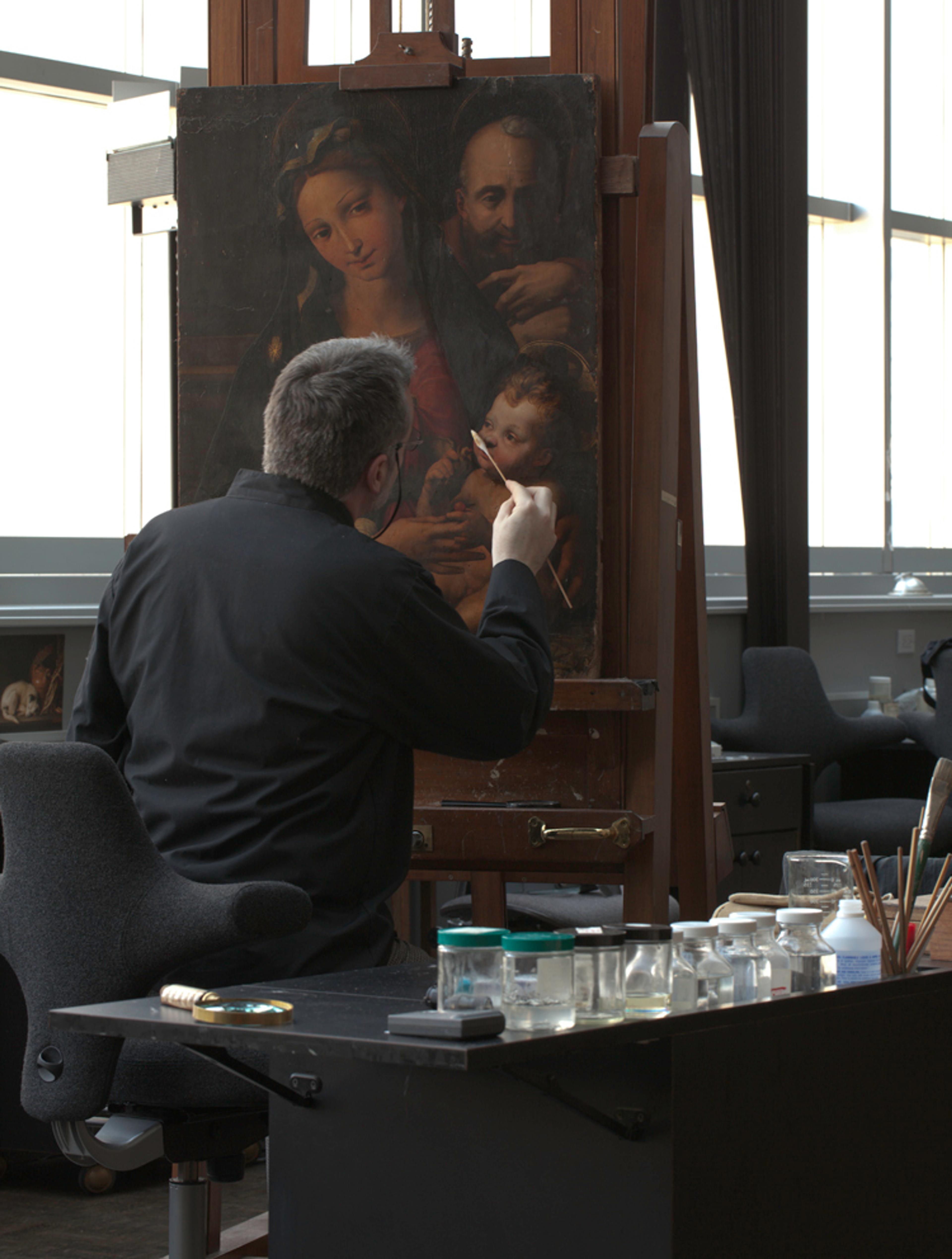 A man works with his back turned to conserve an oil painting.