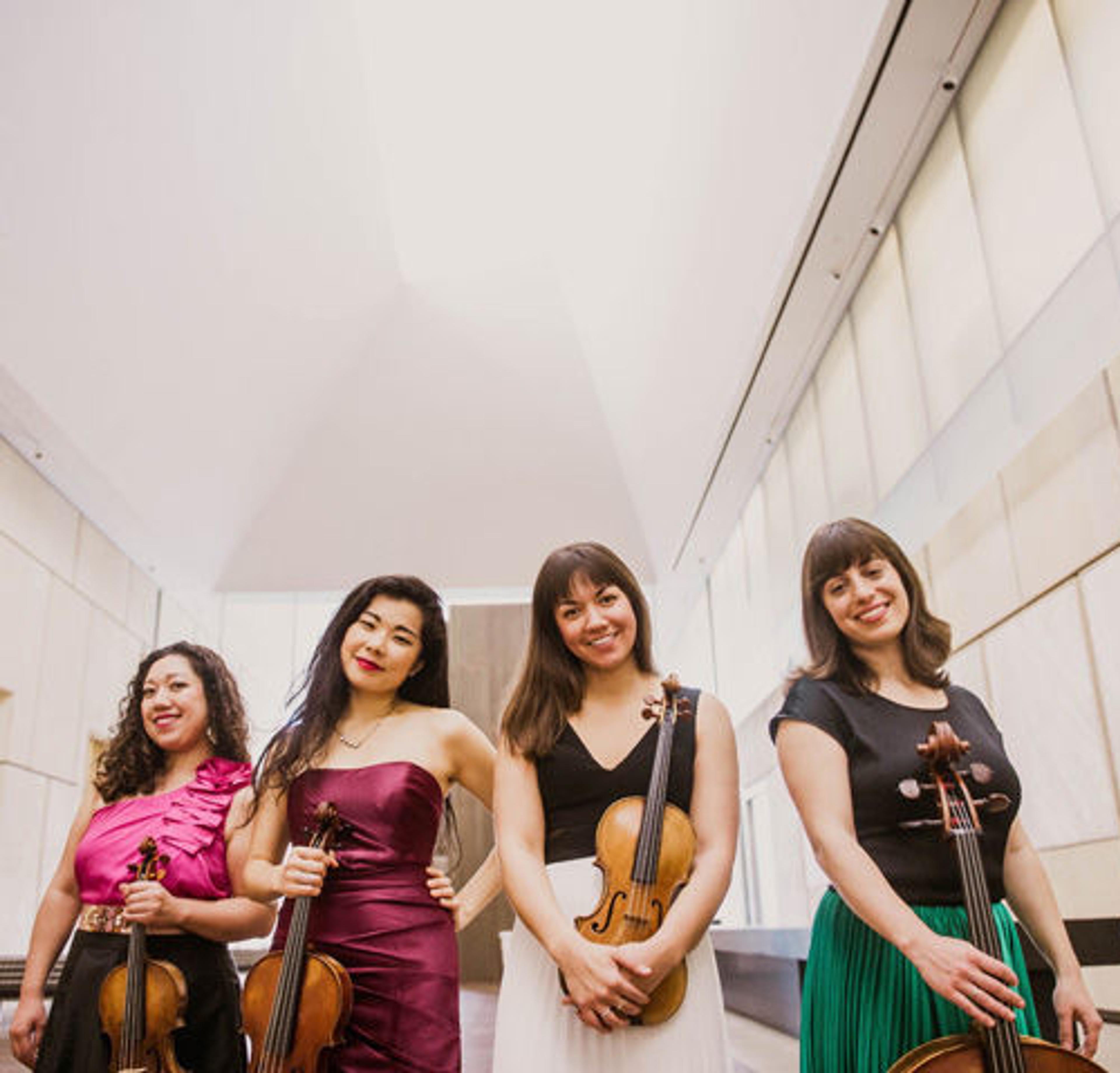 Aizuri Quartet holding their instruments in a large, bright gallery space