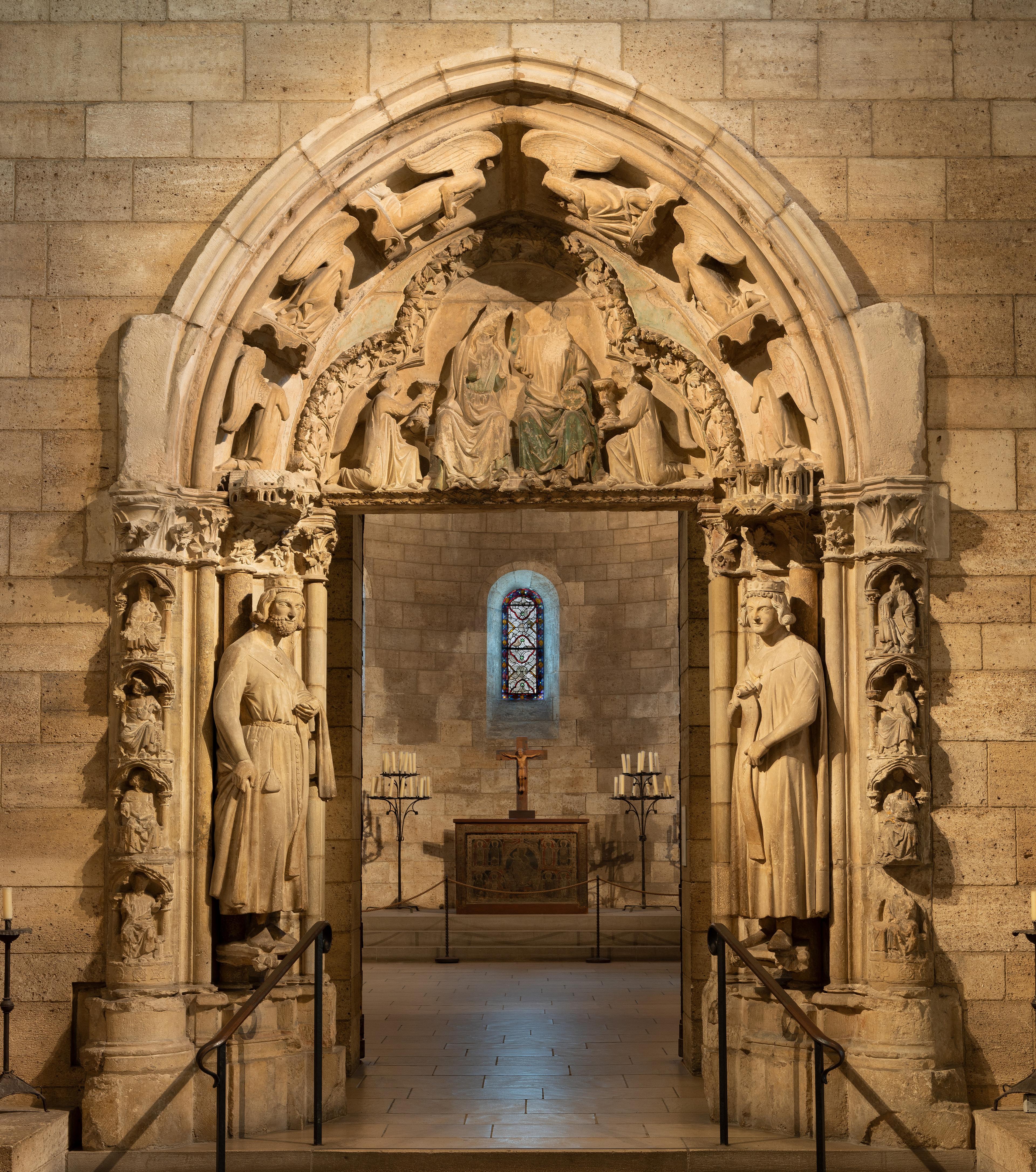 Dramatic stone archway in the Cloisters. Two men flank either side of the doorway, and each have seated religious figures alongside their frames. An archway above shows the coronation of the Virgin.