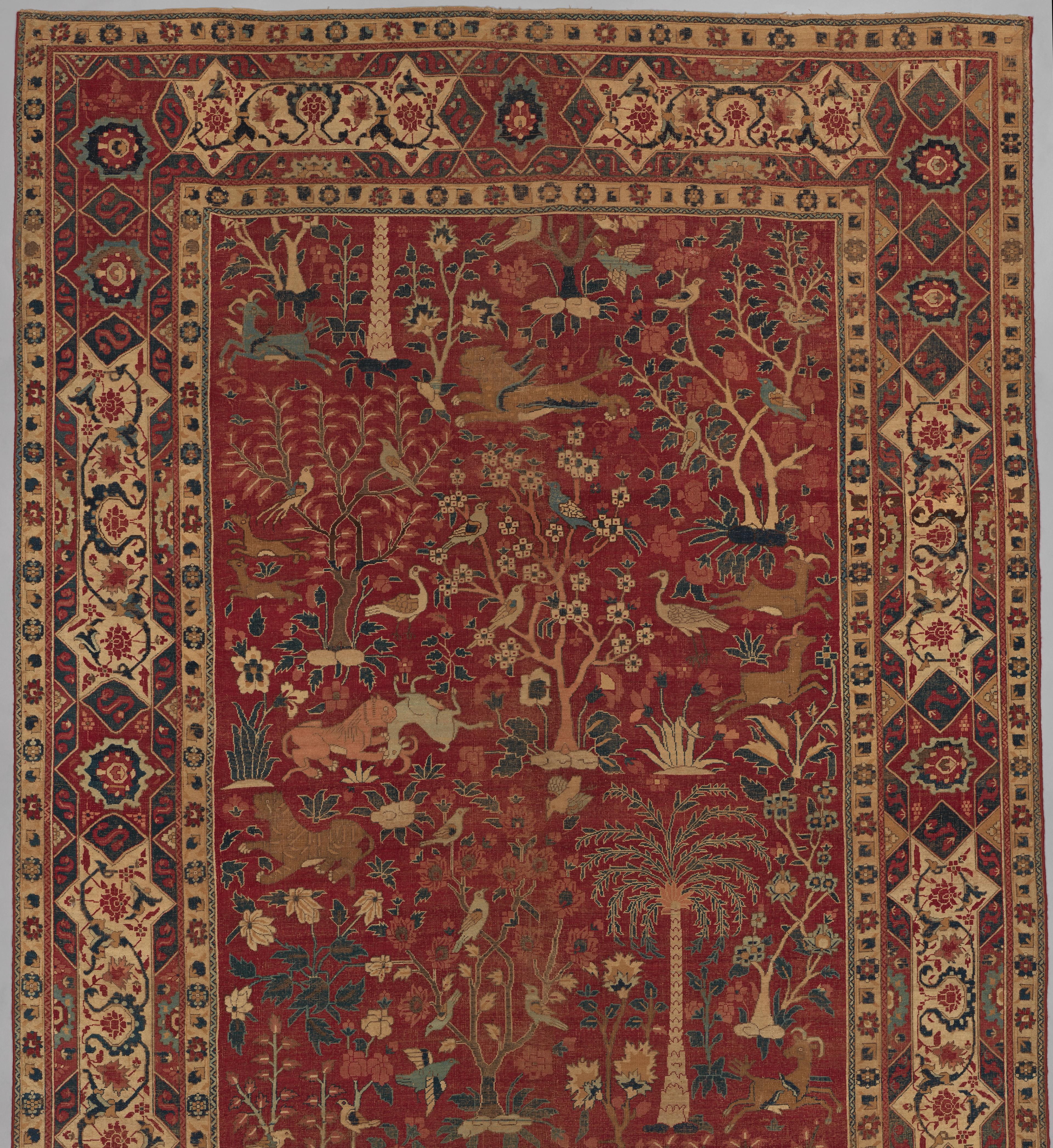 A richly patterned red carpet featuring animals, trees, and floral motifs, bordered by geometric designs.