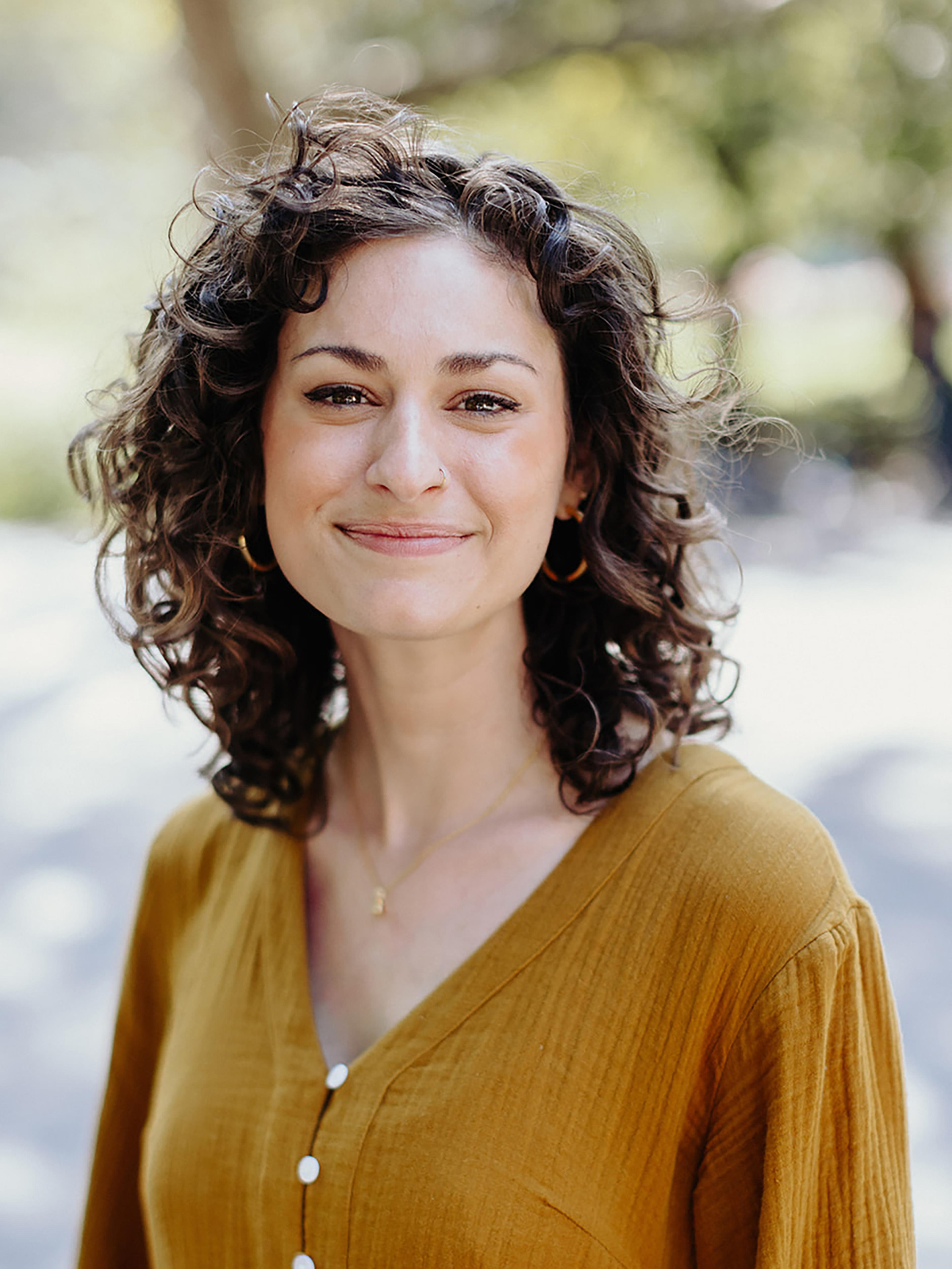 A woman wearing a yellow dress smiles in a sunny park