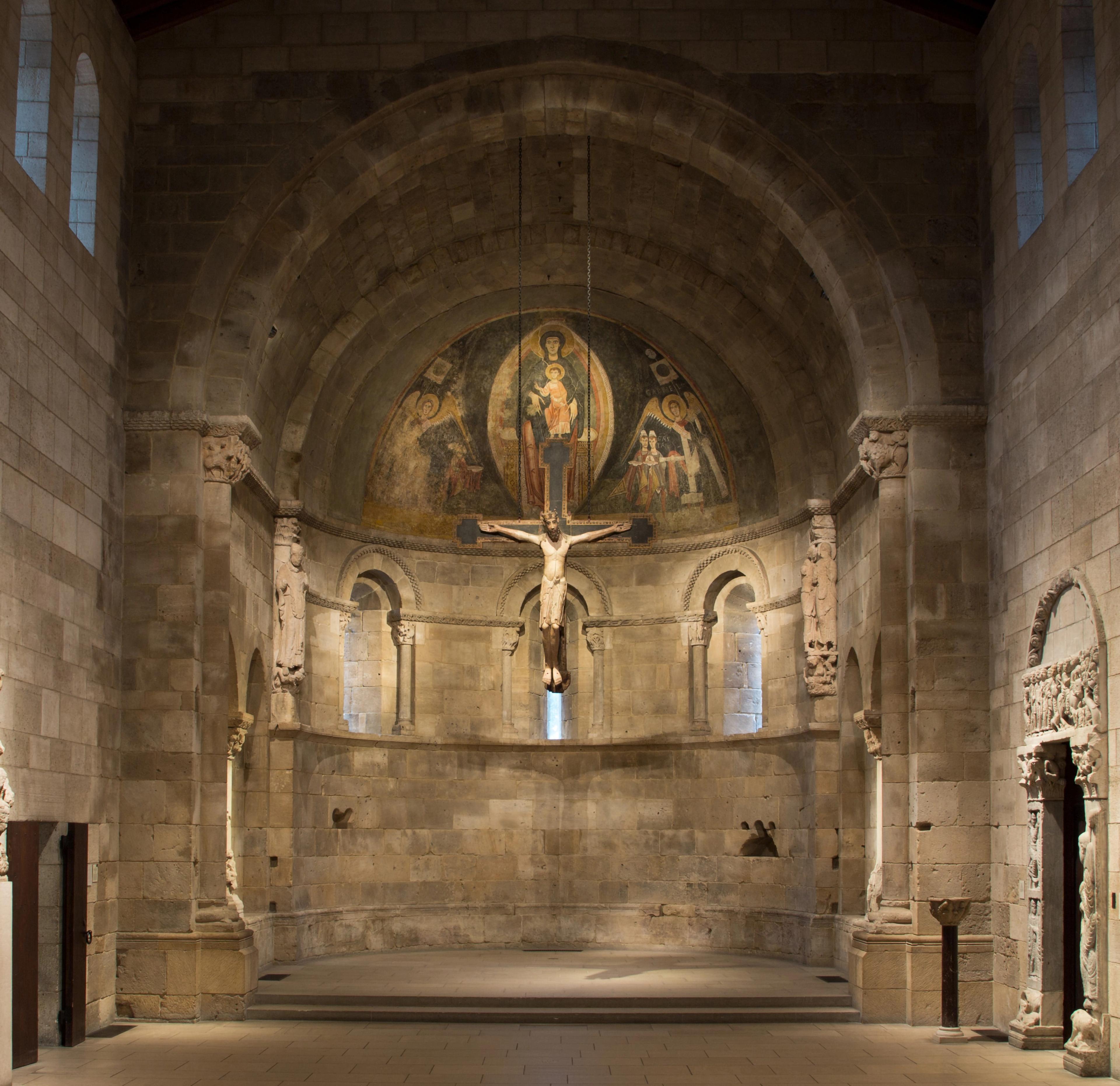 The Met Cloister's Fuentidueña Chapel. Horizontal rows of stone give way to three narrow, arched windows, a vibrant fresco, and a handing figure of Jesus Christ.