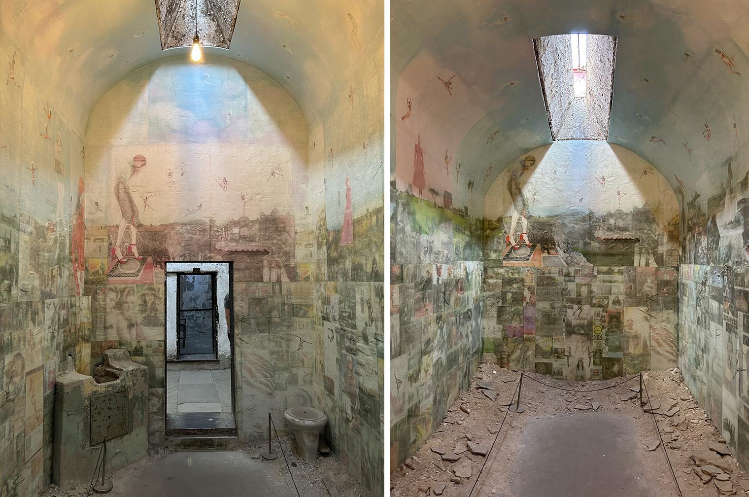 A narrow, arch-ceilinged room with illustrated murals of people and landscapes on the walls. Sunlight streams through a skylight, causing a stark contrast in lighting. An open doorway leads to another section. The floor is littered with broken stone pieces, and there's a vintage sink and toilet visible. The atmosphere feels aged and artistic.