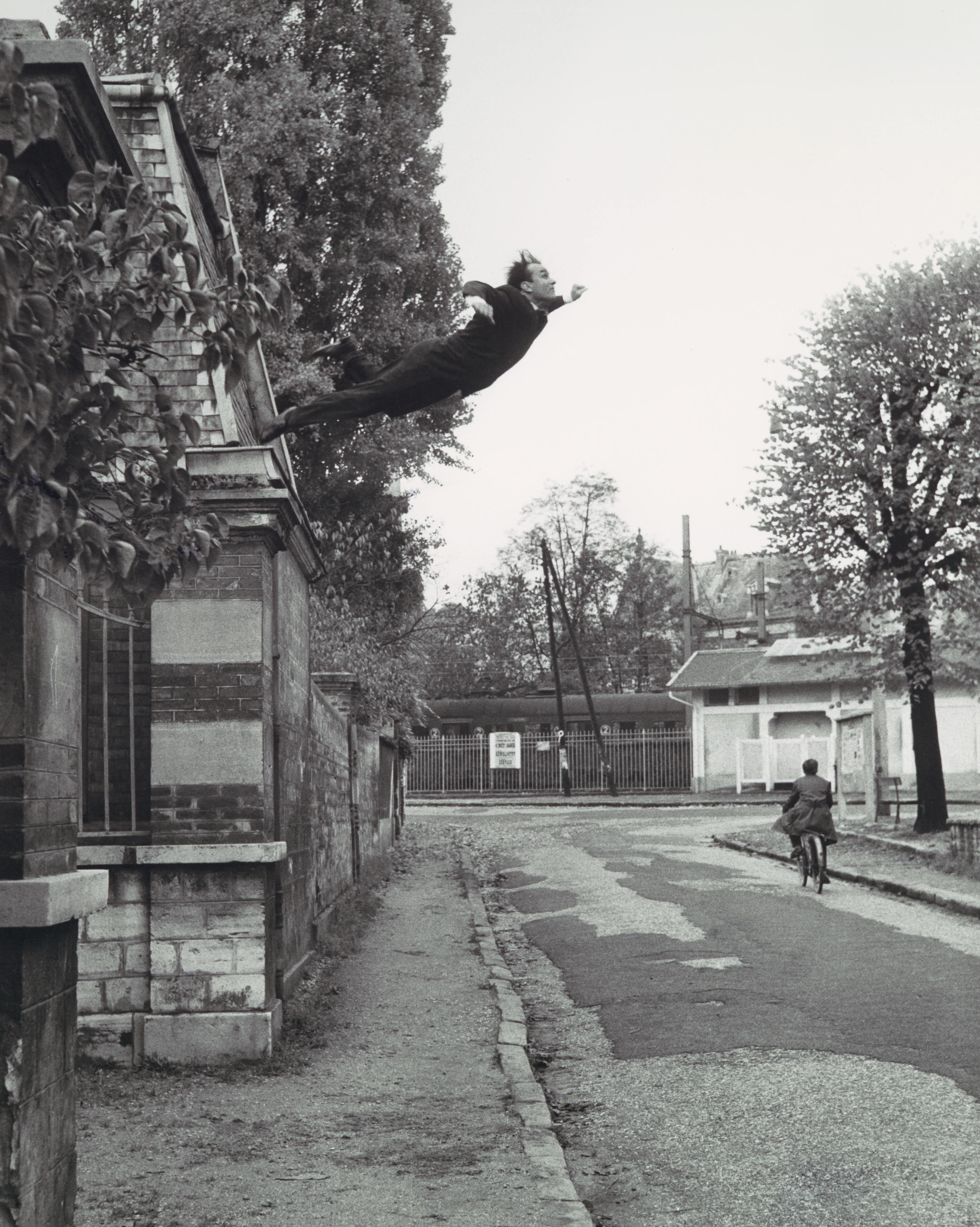 Black-and-white photograph of a man, body outstretched, as he falls gracefully from the roof of a residential building.