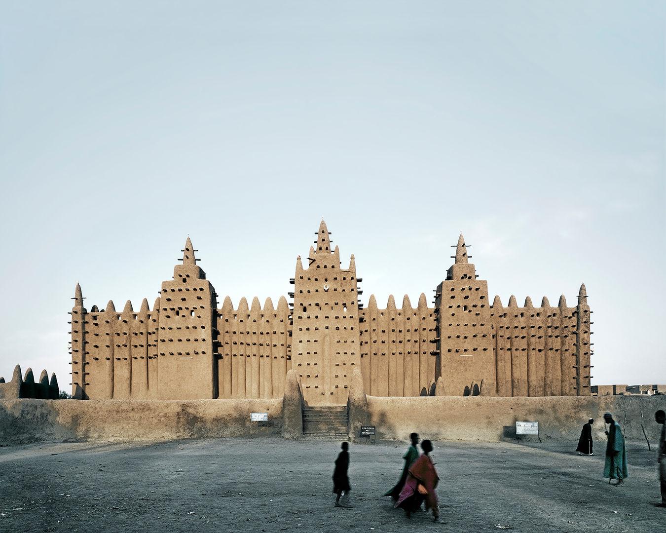 A picture of people walking in front of a great mud mosque