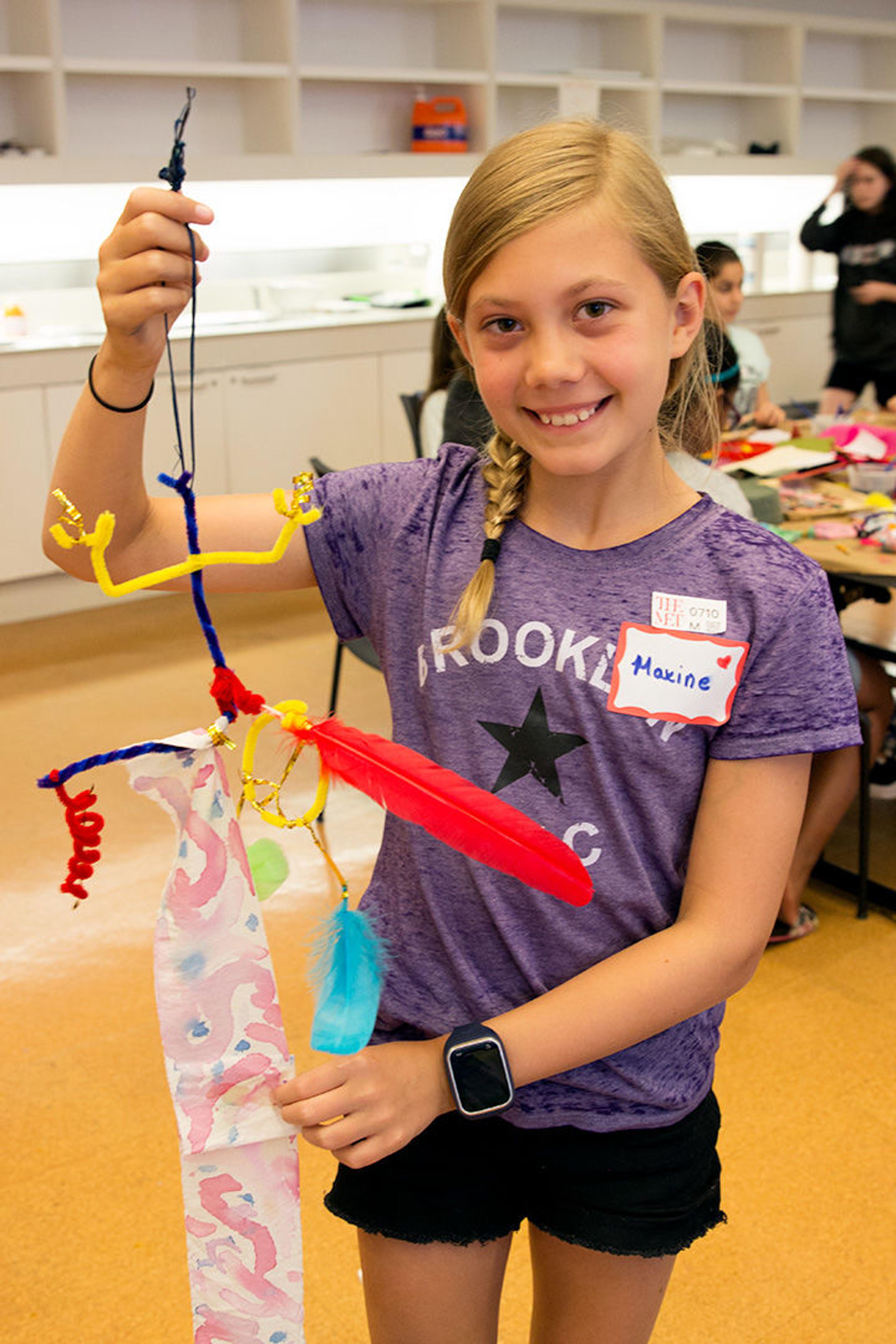 Max holds up her finished mobile made of dyed cloth, pipe cleaners, string, and other materials.