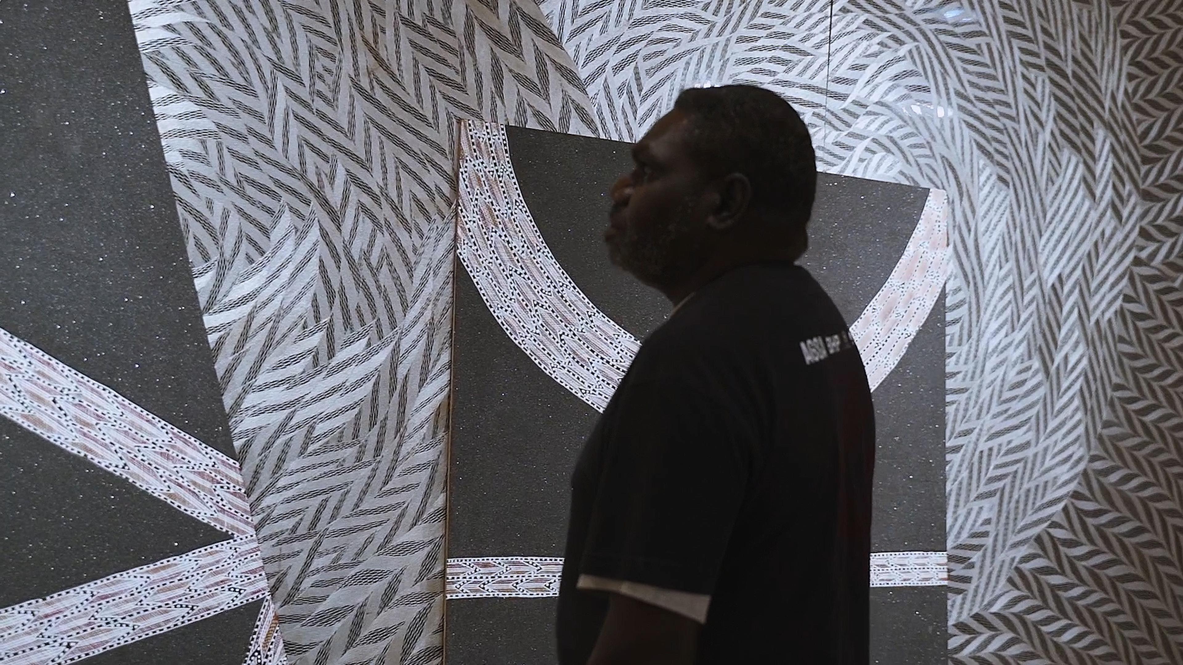 Man standing, surrounded by artwork with swirling, geometric designs