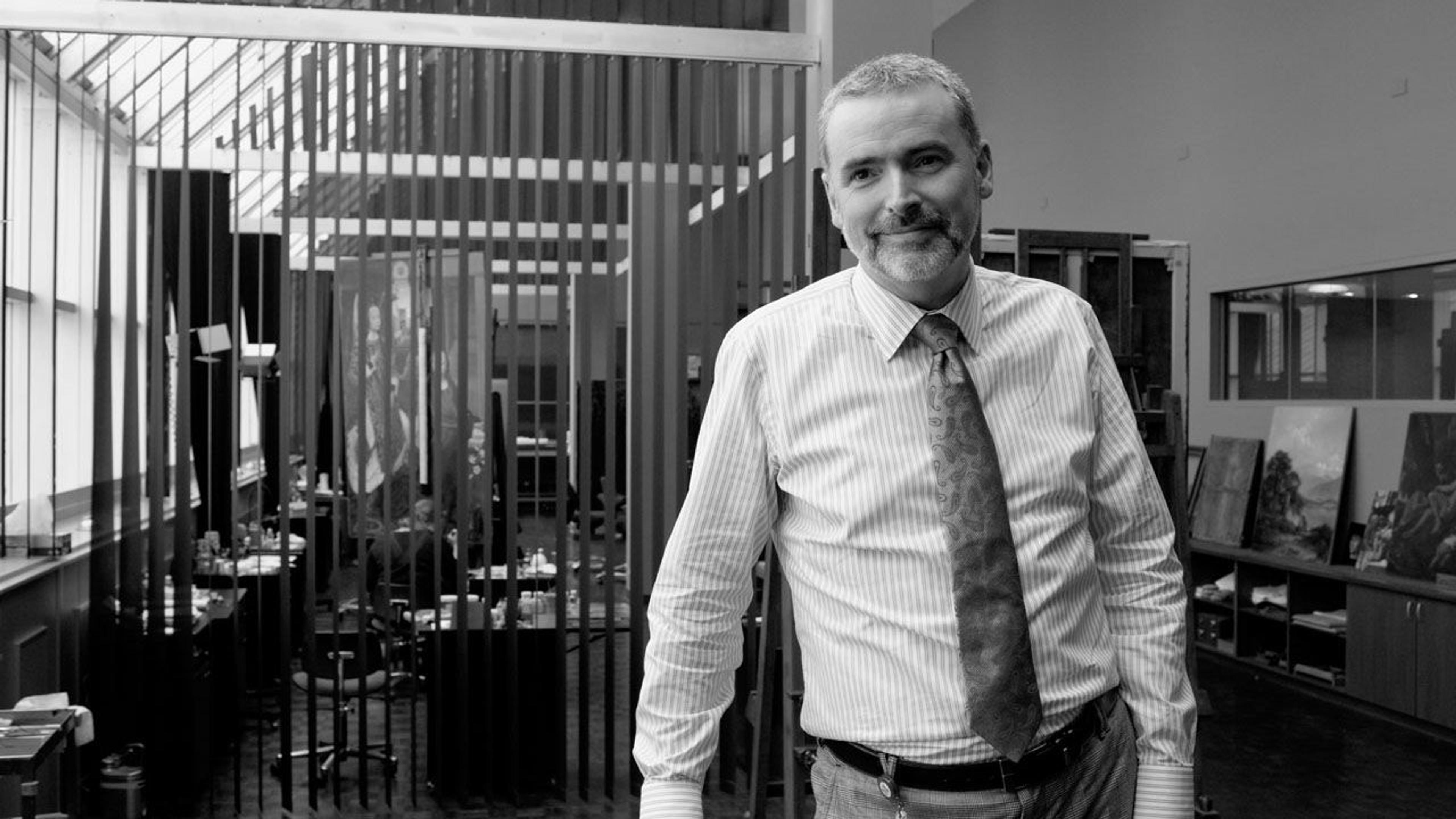 Black and white photograph of paintings conservator Michael Gallagher standing in the paintings conservation studio at The Met