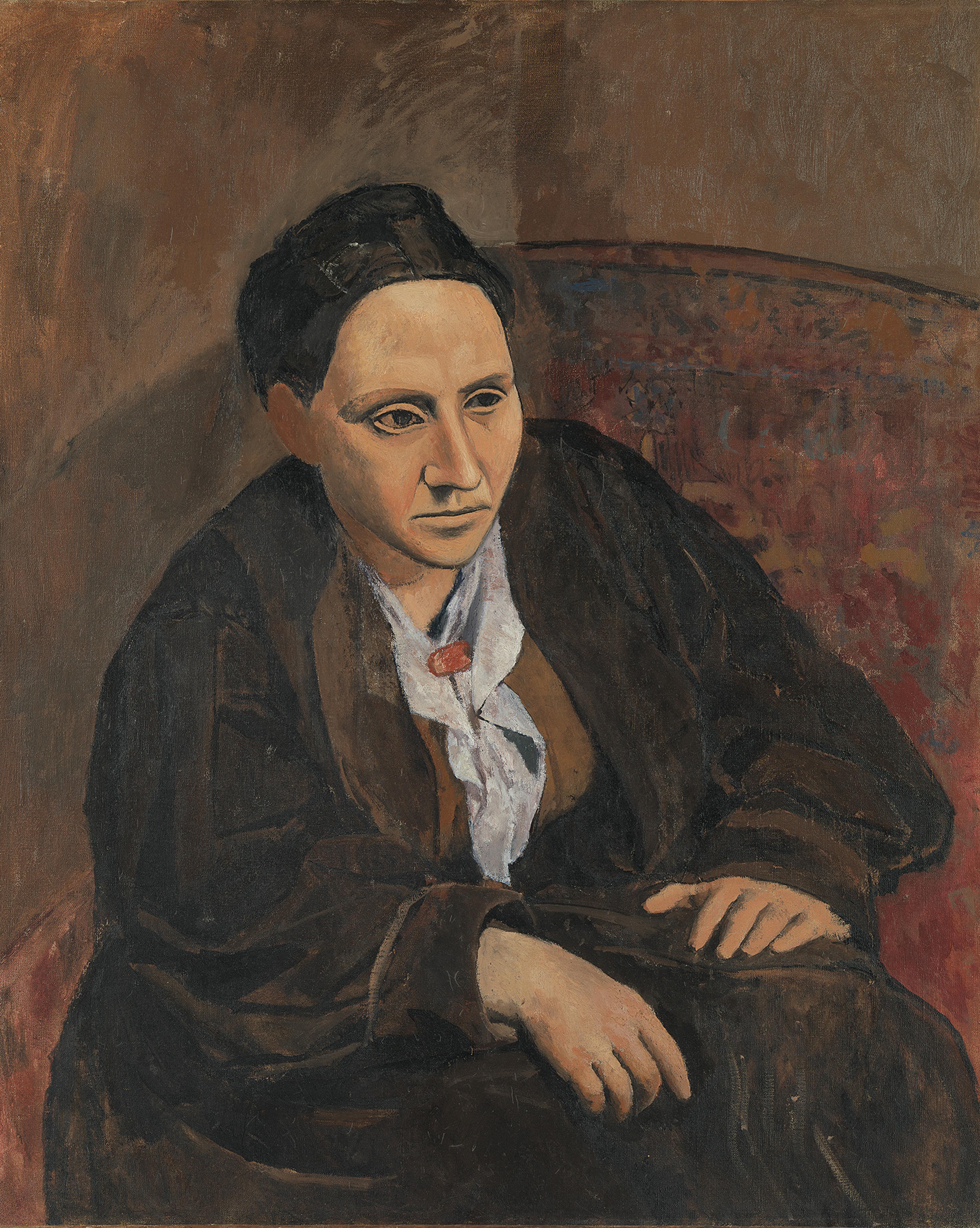 ortrait of Gertrude Stein seated in a patterned chair, wearing dark clothing and a red brooch.
