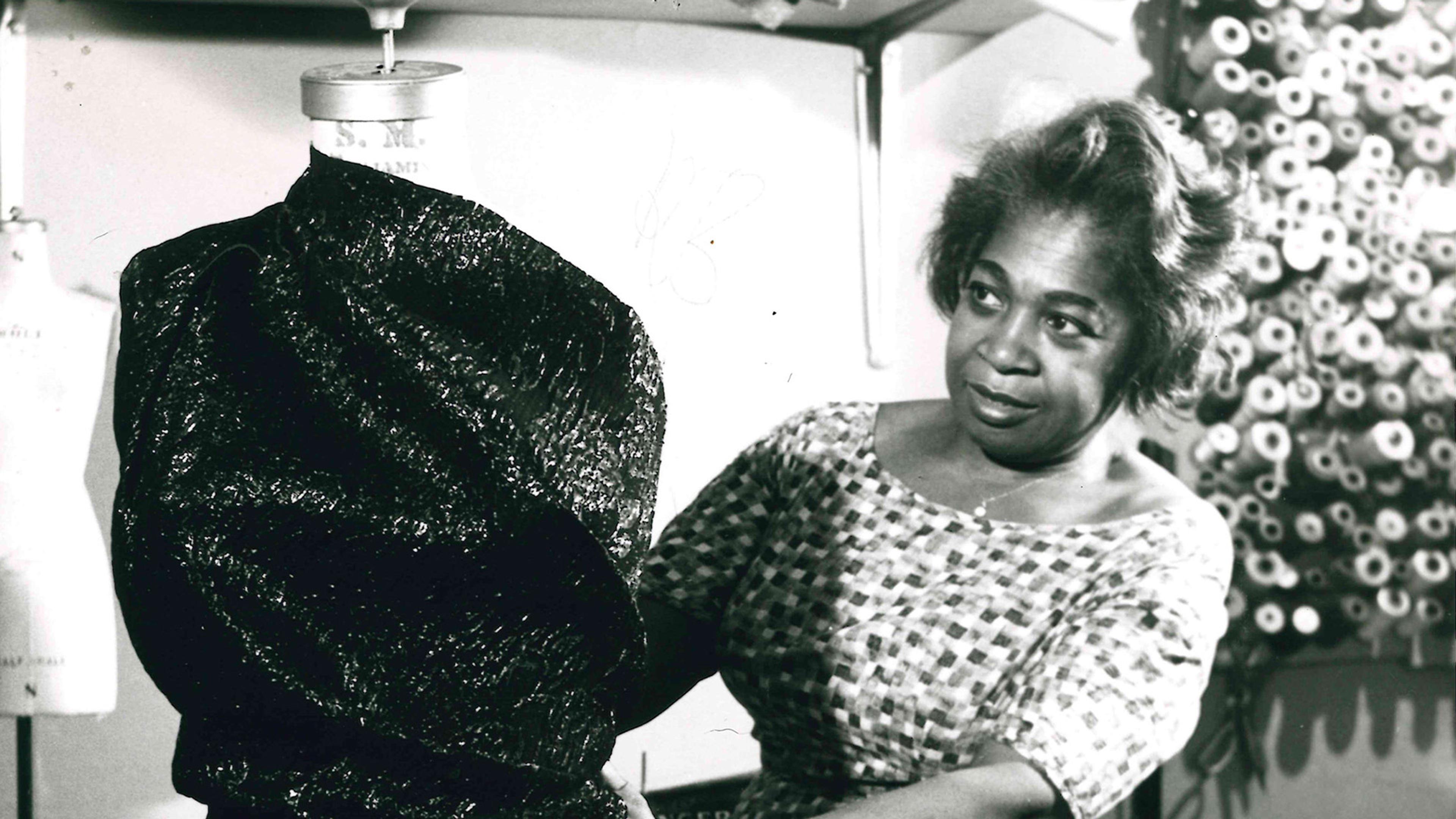 Image of seamstress examining the garment wrapped around tall mannequin.