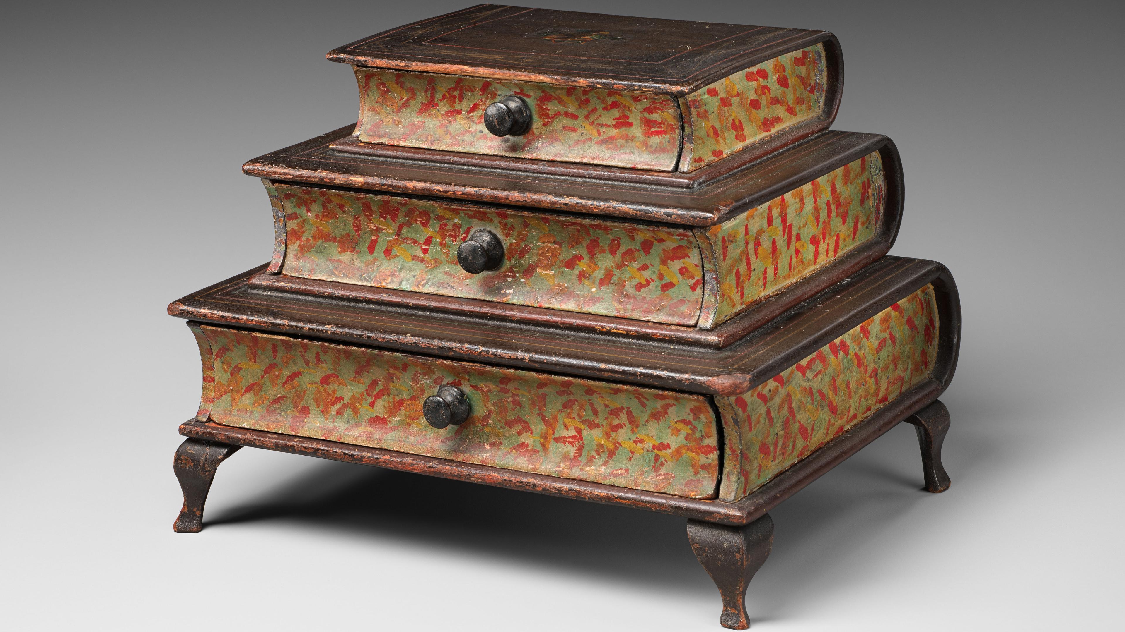 A set of three antique, graduated, stackable wooden boxes, each with a curved lid, painted in a distressed red with faint foliage motifs, featuring a central metal pull handle, resting on small, stylized feet.