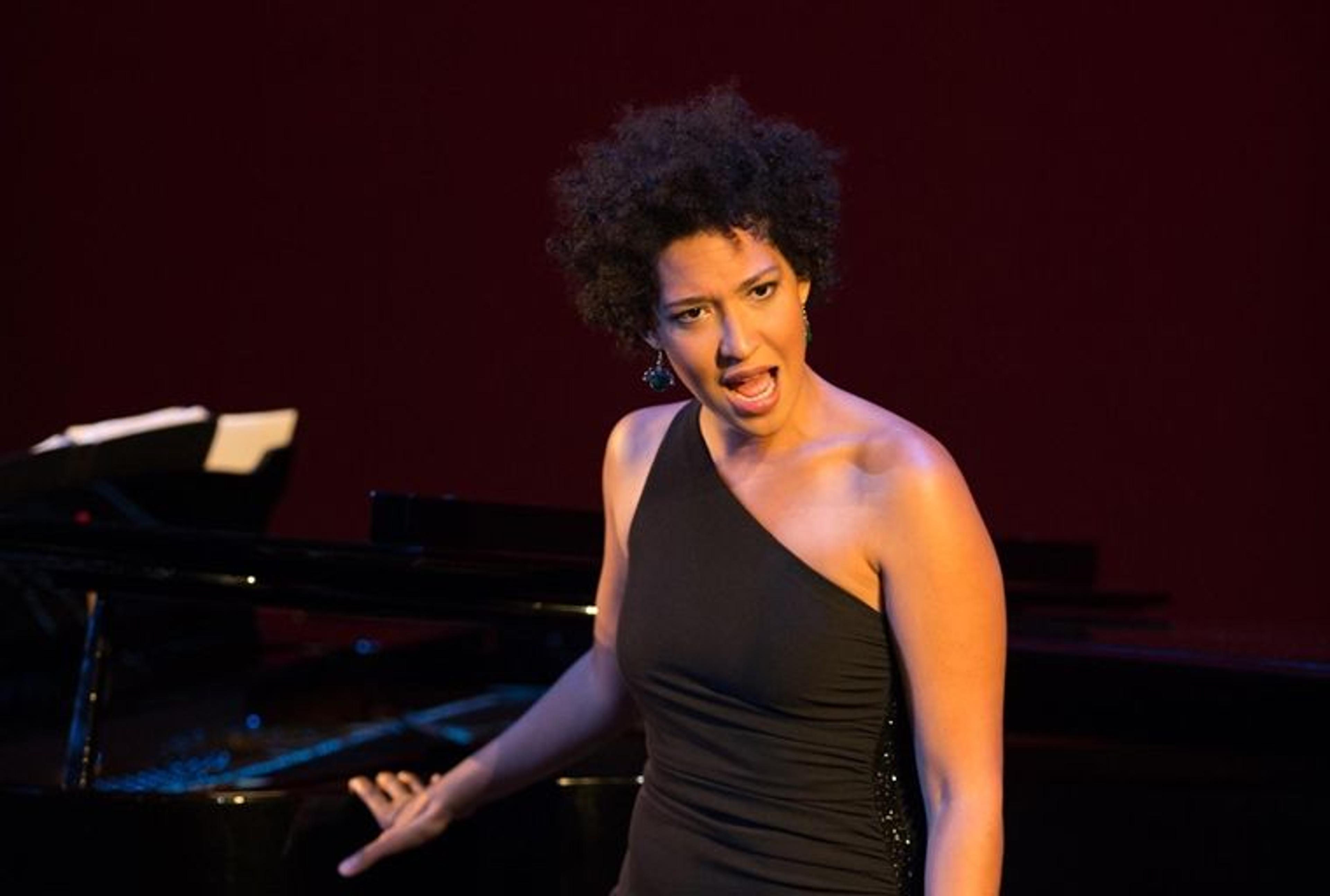 Julia Bullock wearing a black dress and singing in front of a grand piano