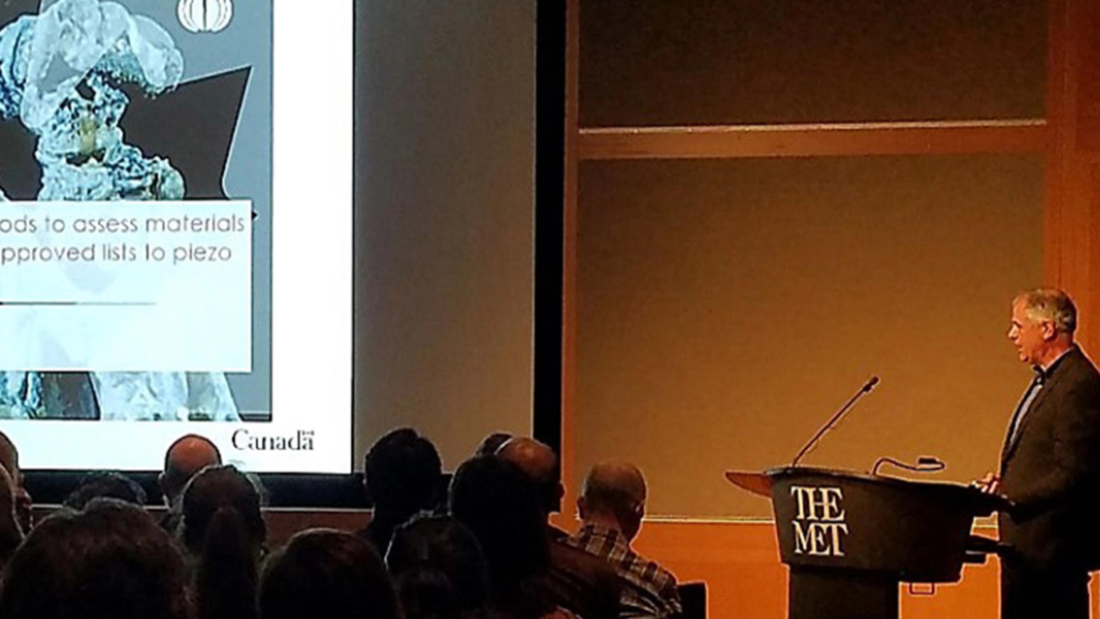 presenter speaks at a podium gives a powerpoint presentation in front of an audience.