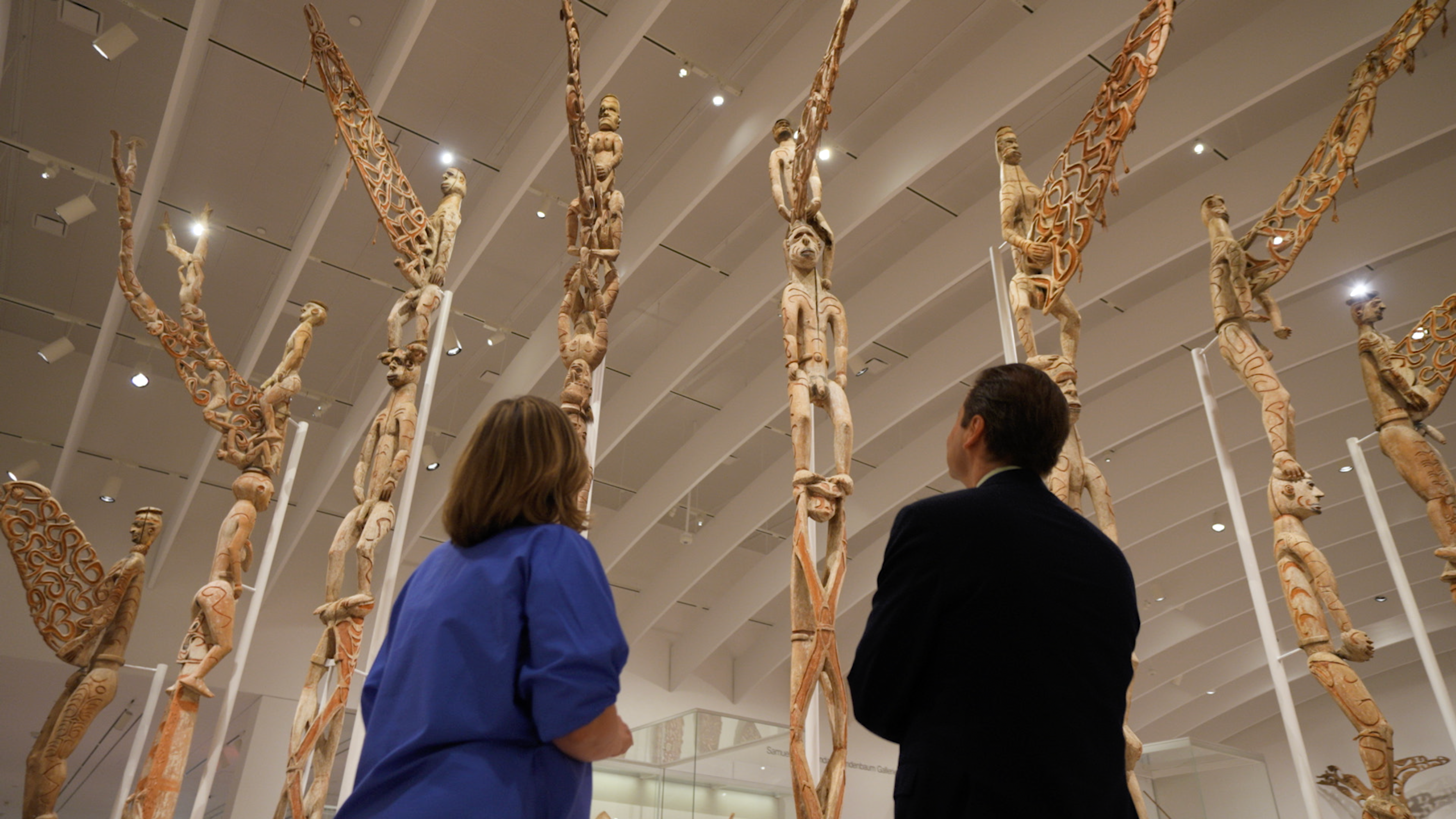 The backs of Maia Nuku and Max Hollein as they look up at Bisj poles in the Arts of Oceania galleries