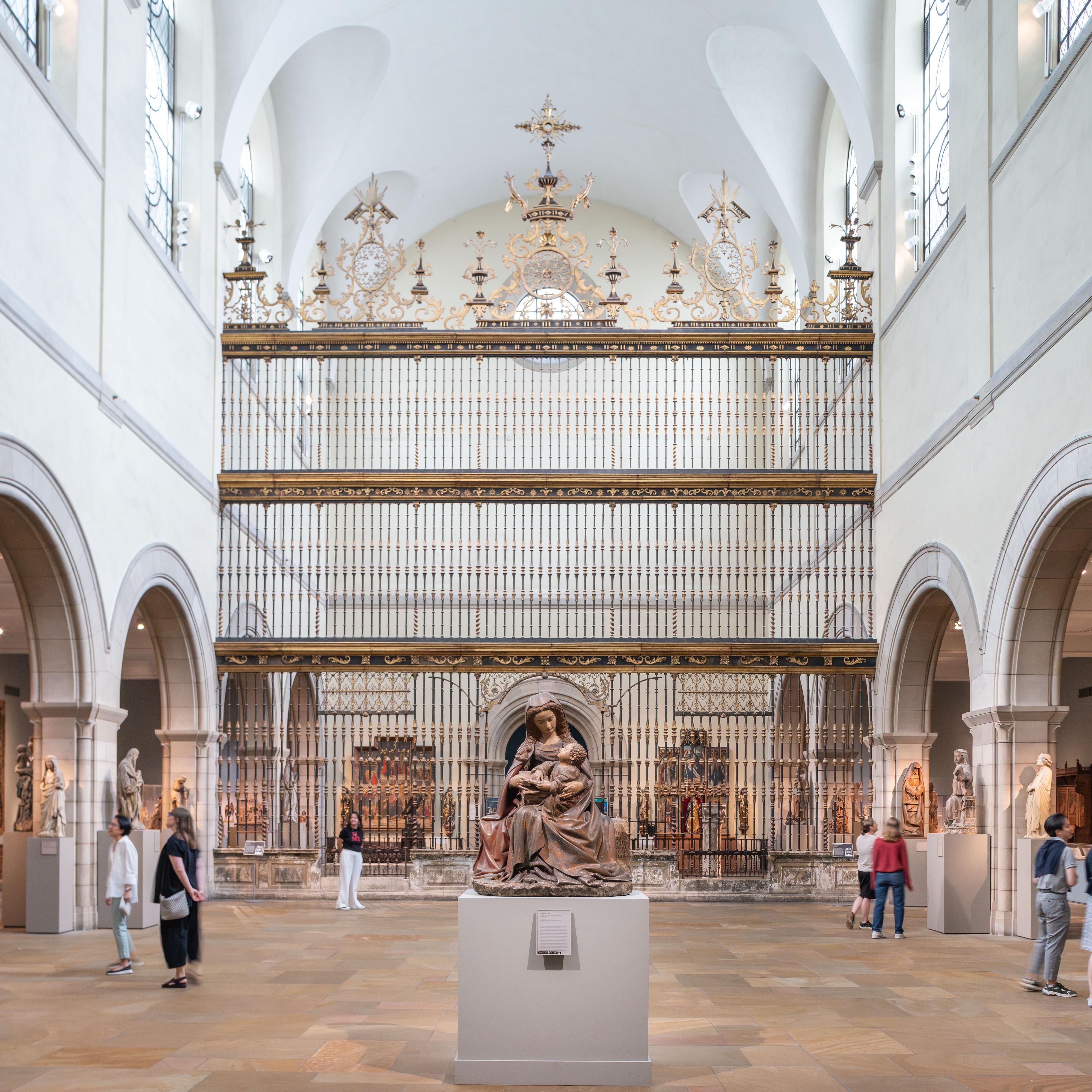 A spacious museum gallery with a Spanish choir screen in the center and filled with large-scale medieval sculptures, altarpieces, tapestries, and furniture.