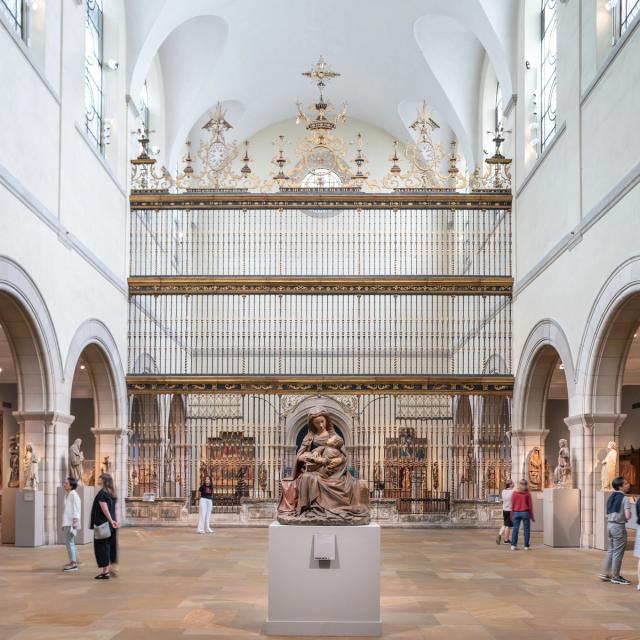 A spacious museum gallery with a Spanish choir screen in the center and filled with large-scale medieval sculptures, altarpieces, tapestries, and furniture.
