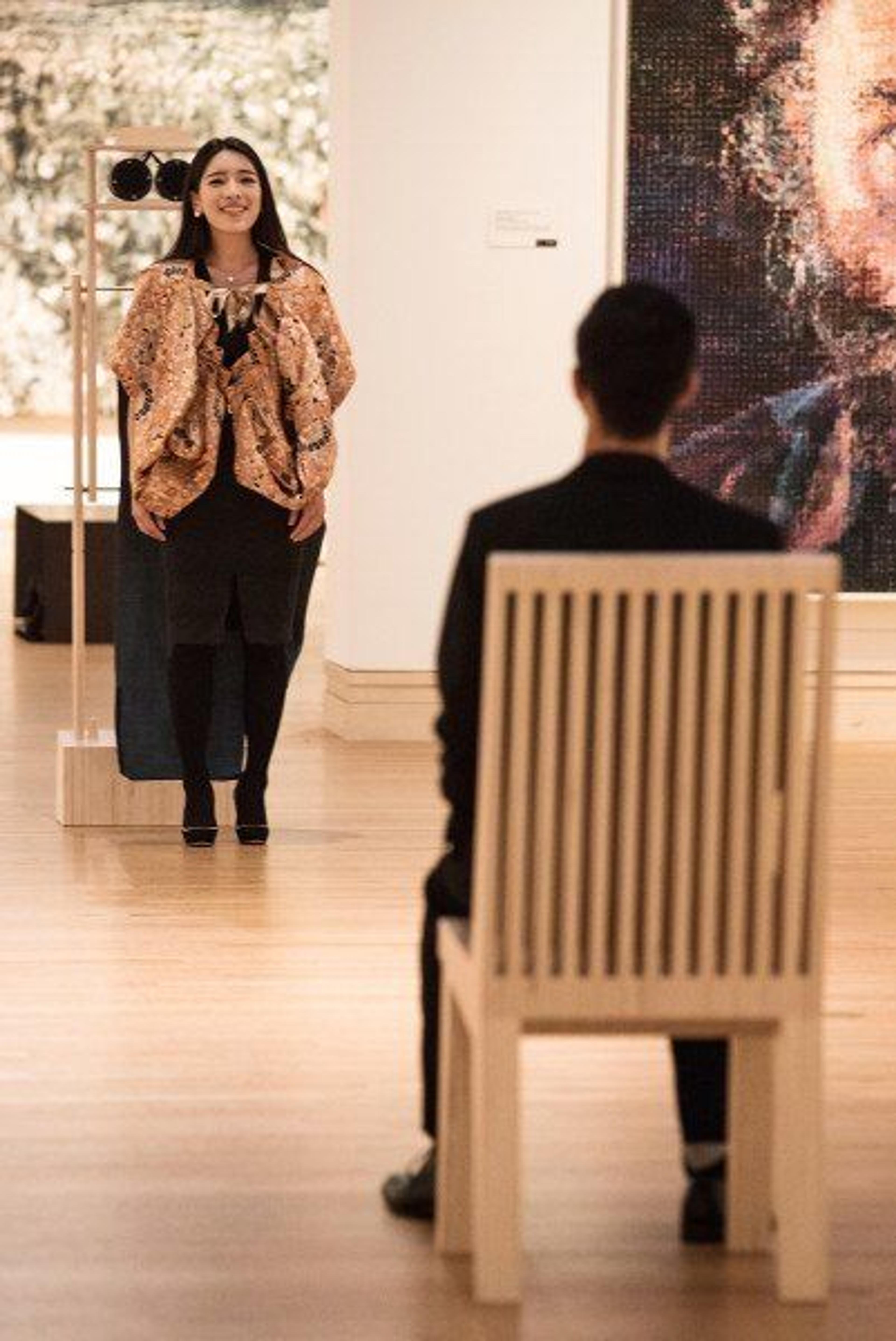 A woman standing in a gallery facing a man seated in a chair