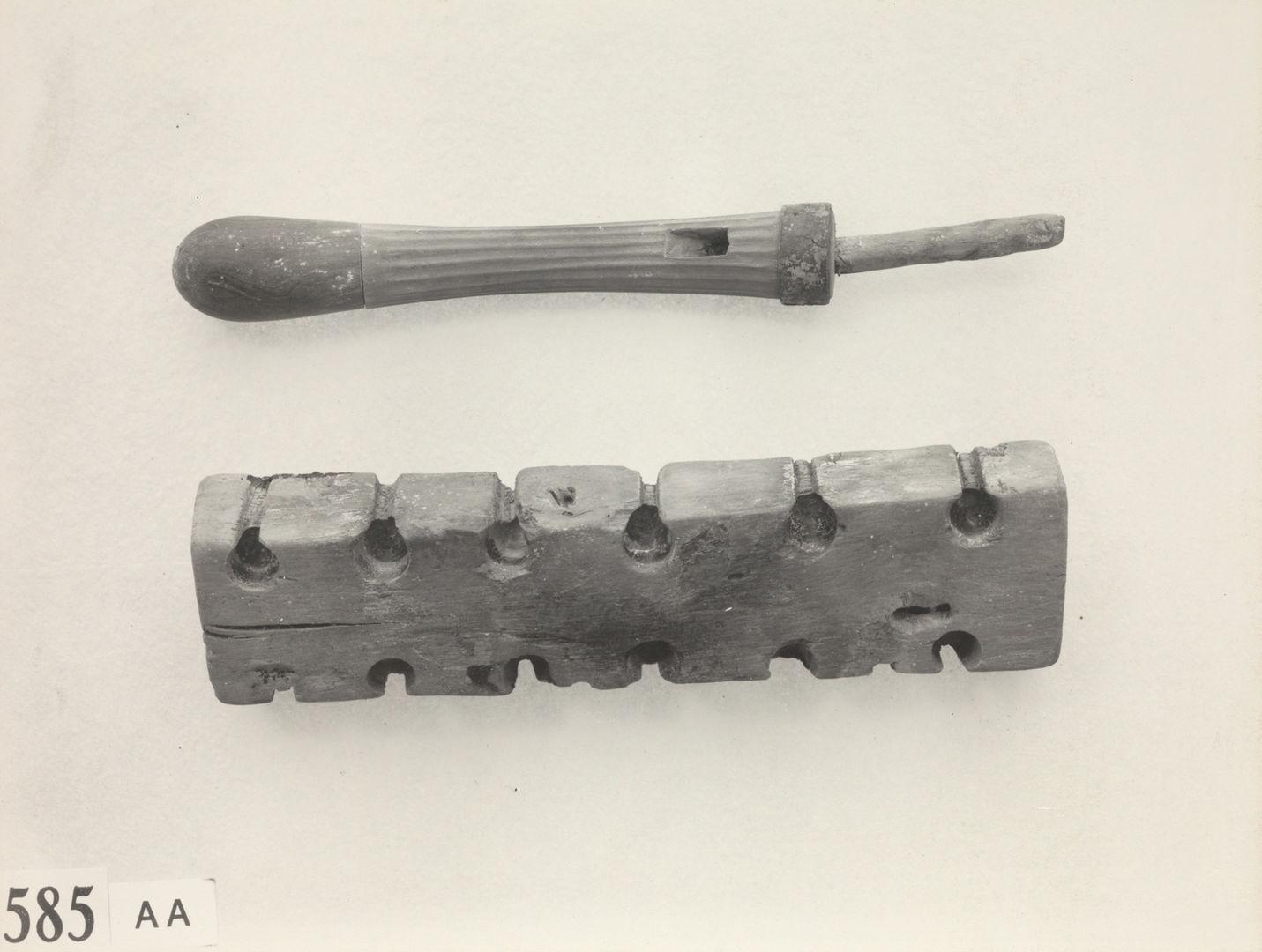 An awl-shaped tool with a blunt tip and a rectangular piece of wood with six small pits on each side, spaced regularly.