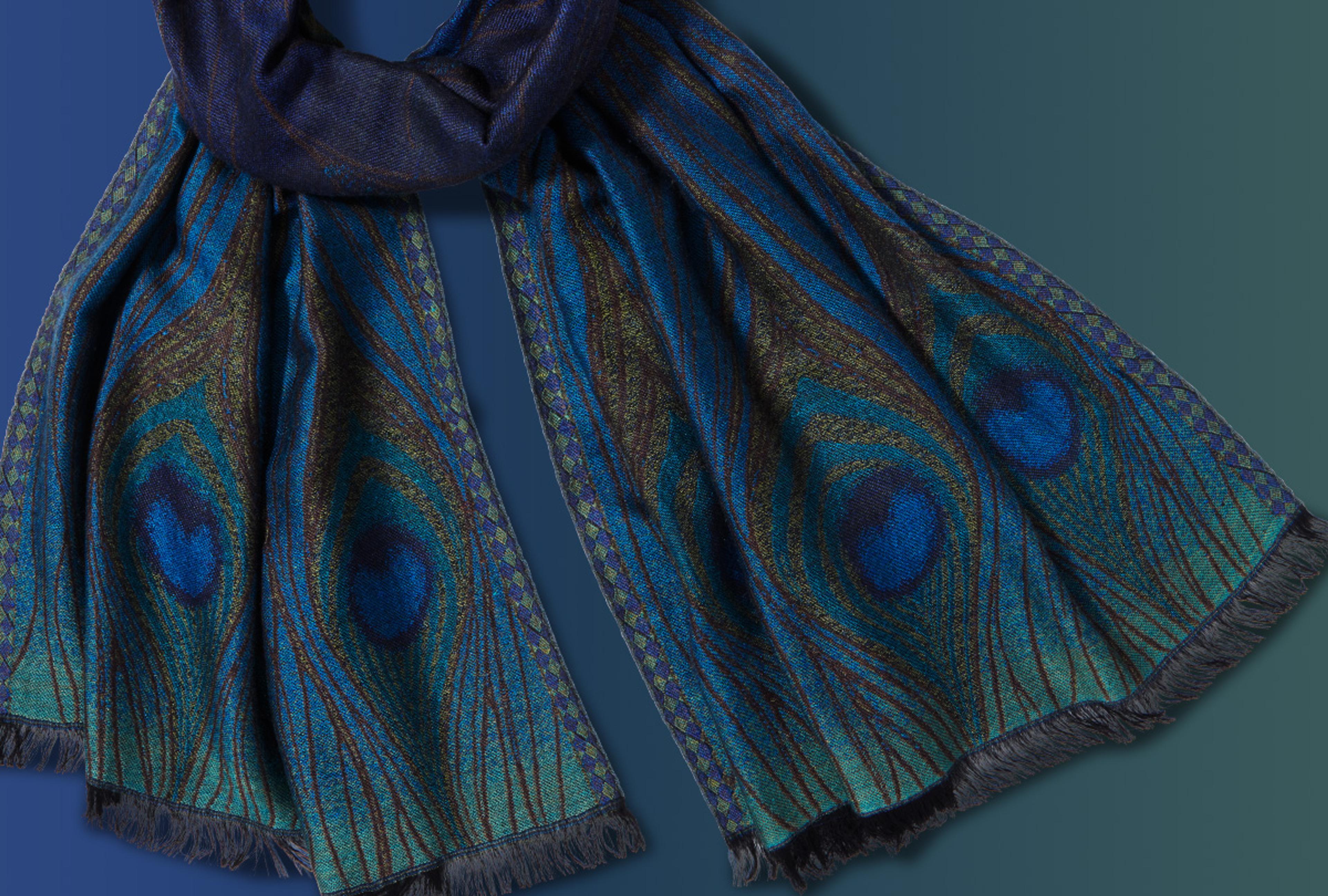 Scarf with peacock feather design photographed against a deep blue and green ombre background.