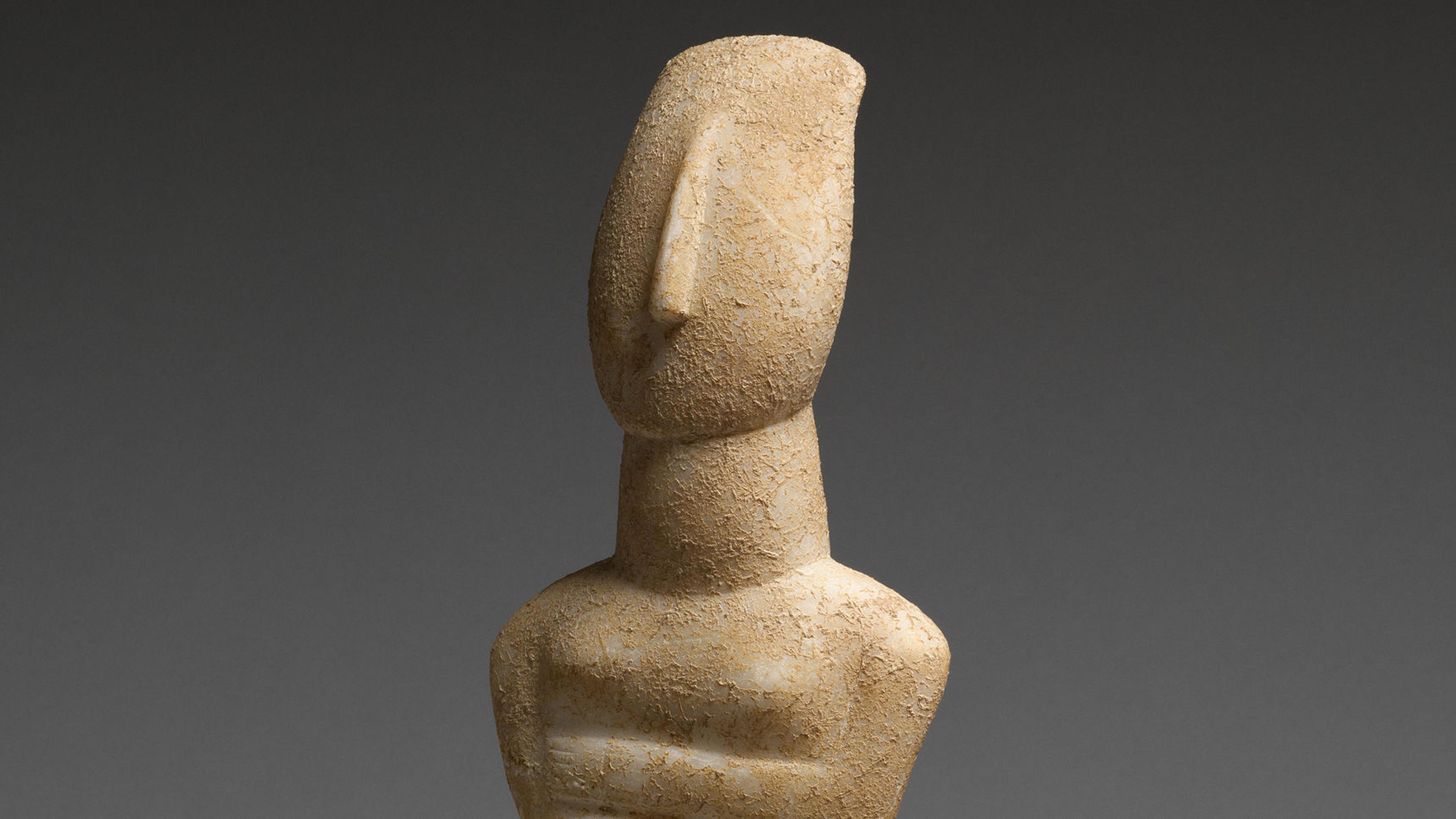 Nude stone Cycladic figure with it's arms crossed against a grey background.