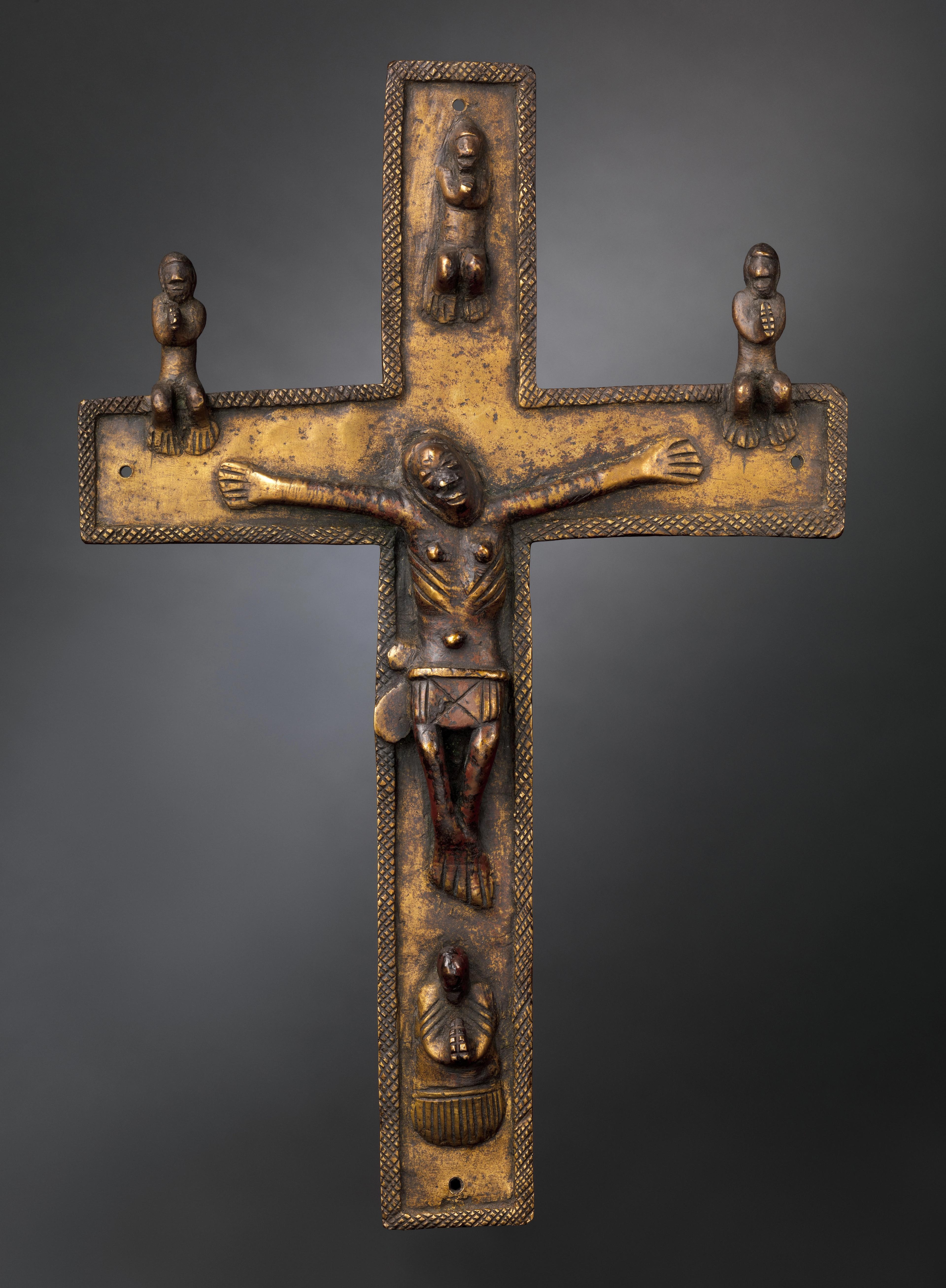 A brass cast crucifix featuring a Christ figure cast in relief, arms extended, with four smaller figures on the apex, base, and arms of the cross.
