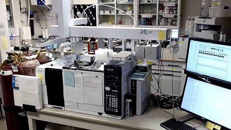 A crowded desk in a scientific laboratory covered with an array of tower-like hardware aligned side by side. Monitors are on the right side of the desk and cabinets in the background hold various materials.