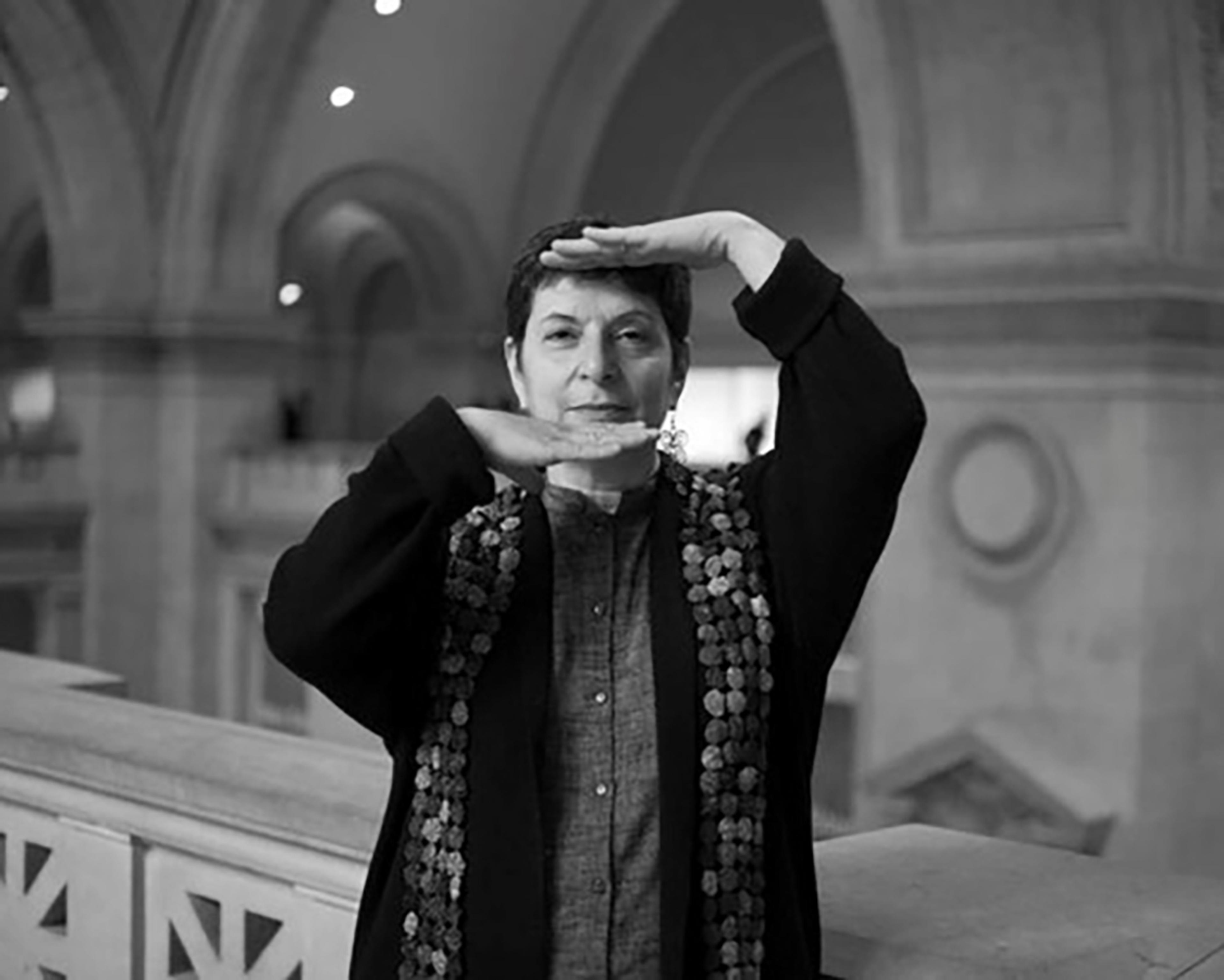 A person stands inside The Met, holding one hand above their head and the other below their chin, palms facing each other in a black and white photo.