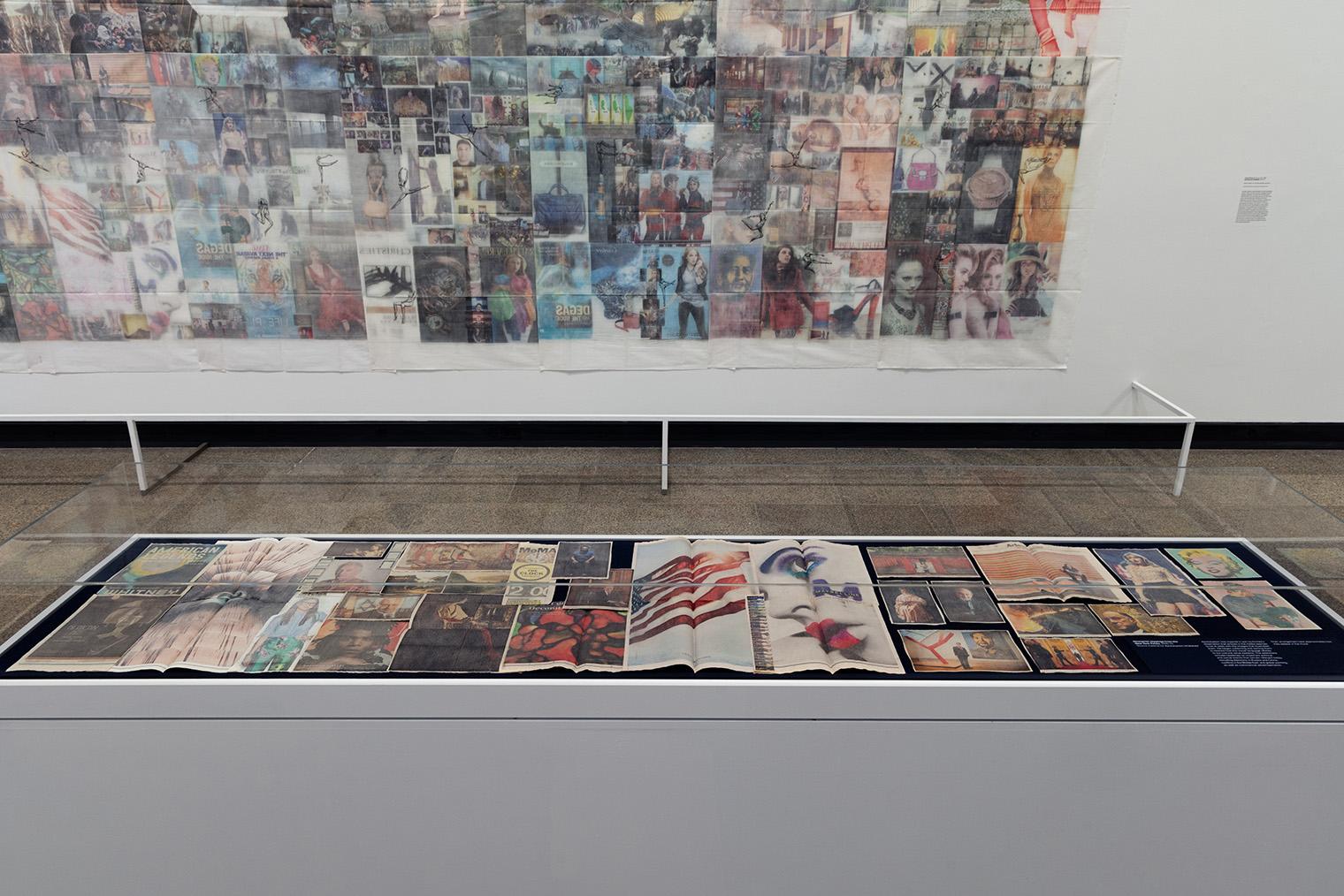 A collage of magazine covers and images is displayed in a glass case, with a large, blurred mural behind it. The scene conveys a vibrant, artistic tone.