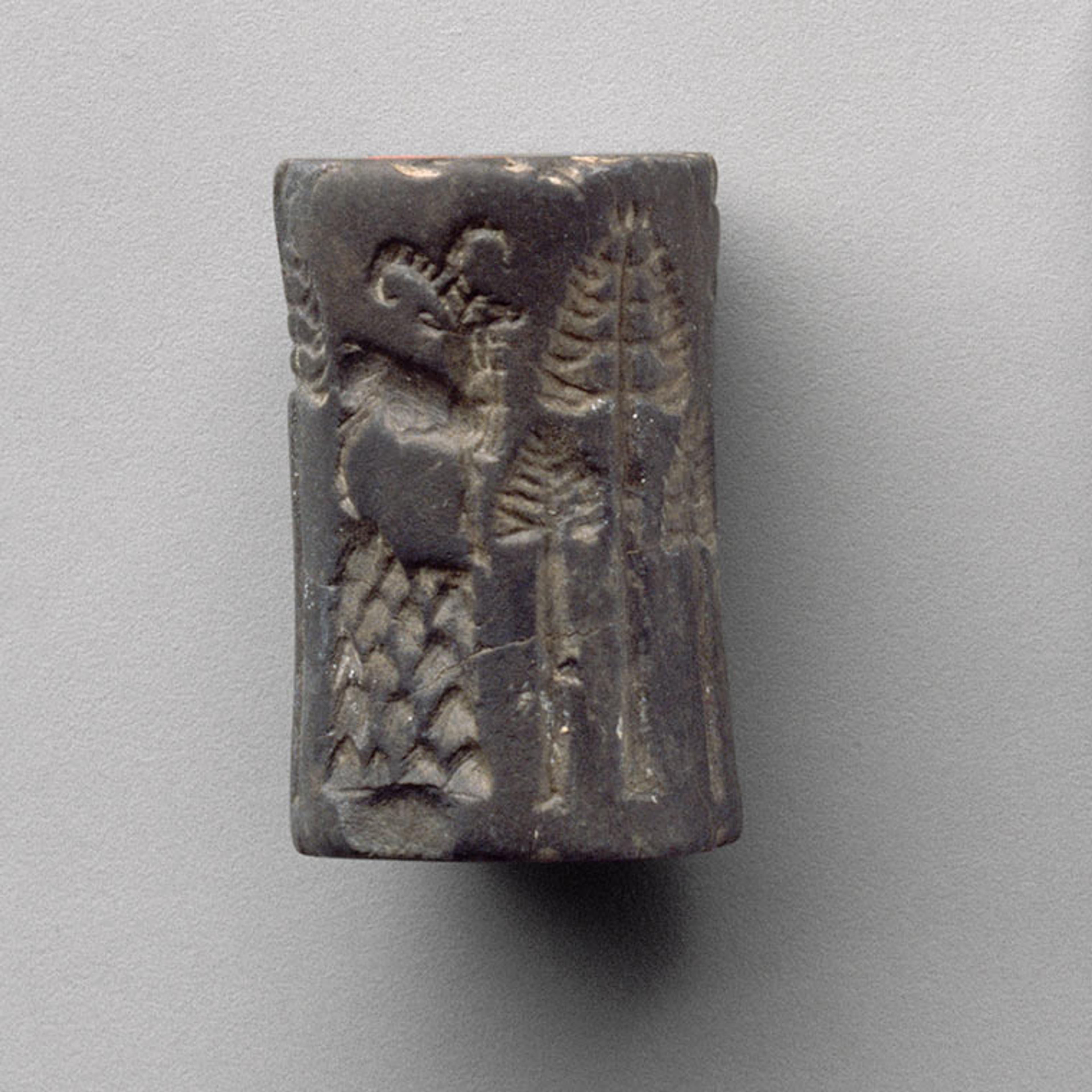 A charcoal-colored cylinder seal on which an ibex is shown next to two trees.