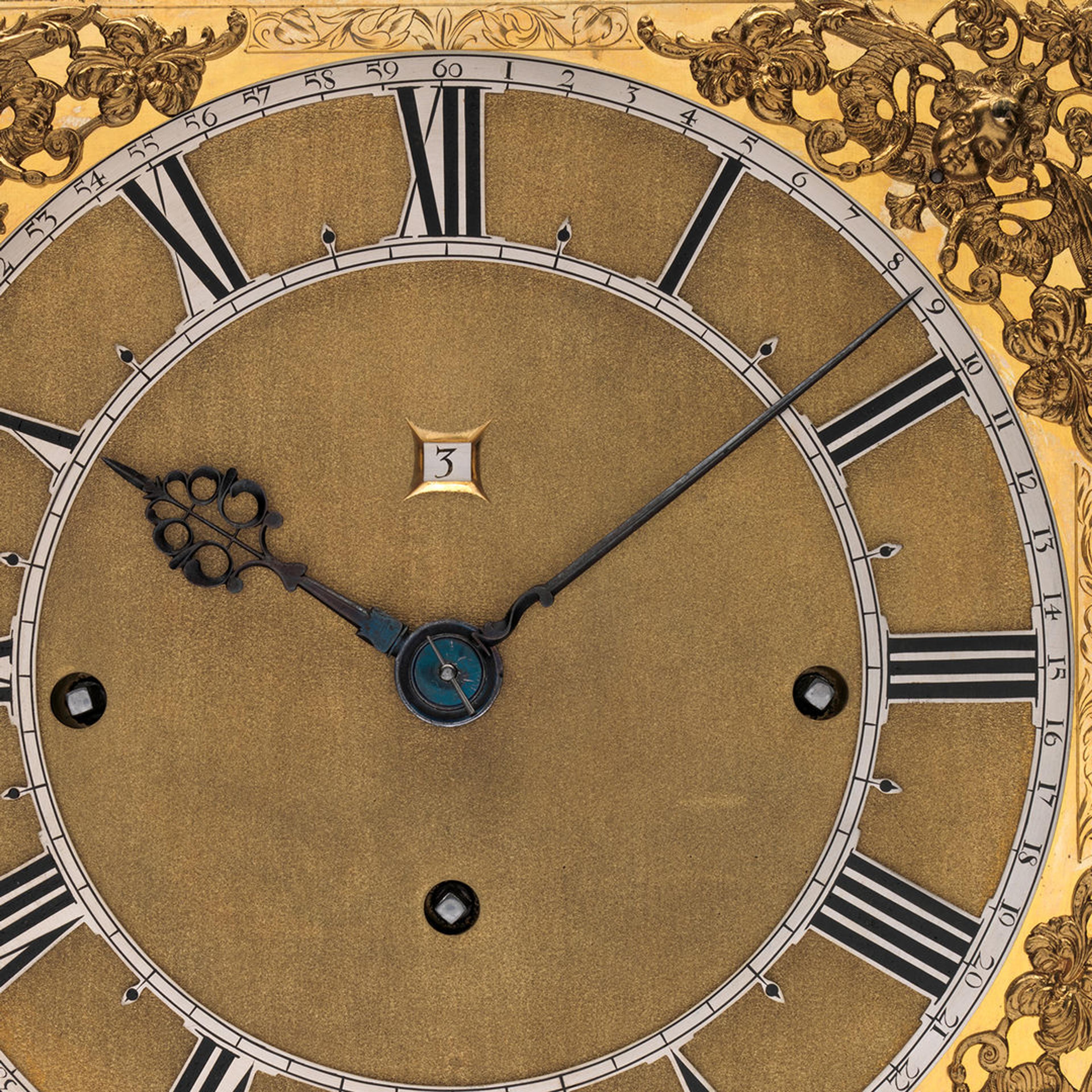 Detail of a clock face with gold-colored accents, roman numeral numbers, and a counter for the date.