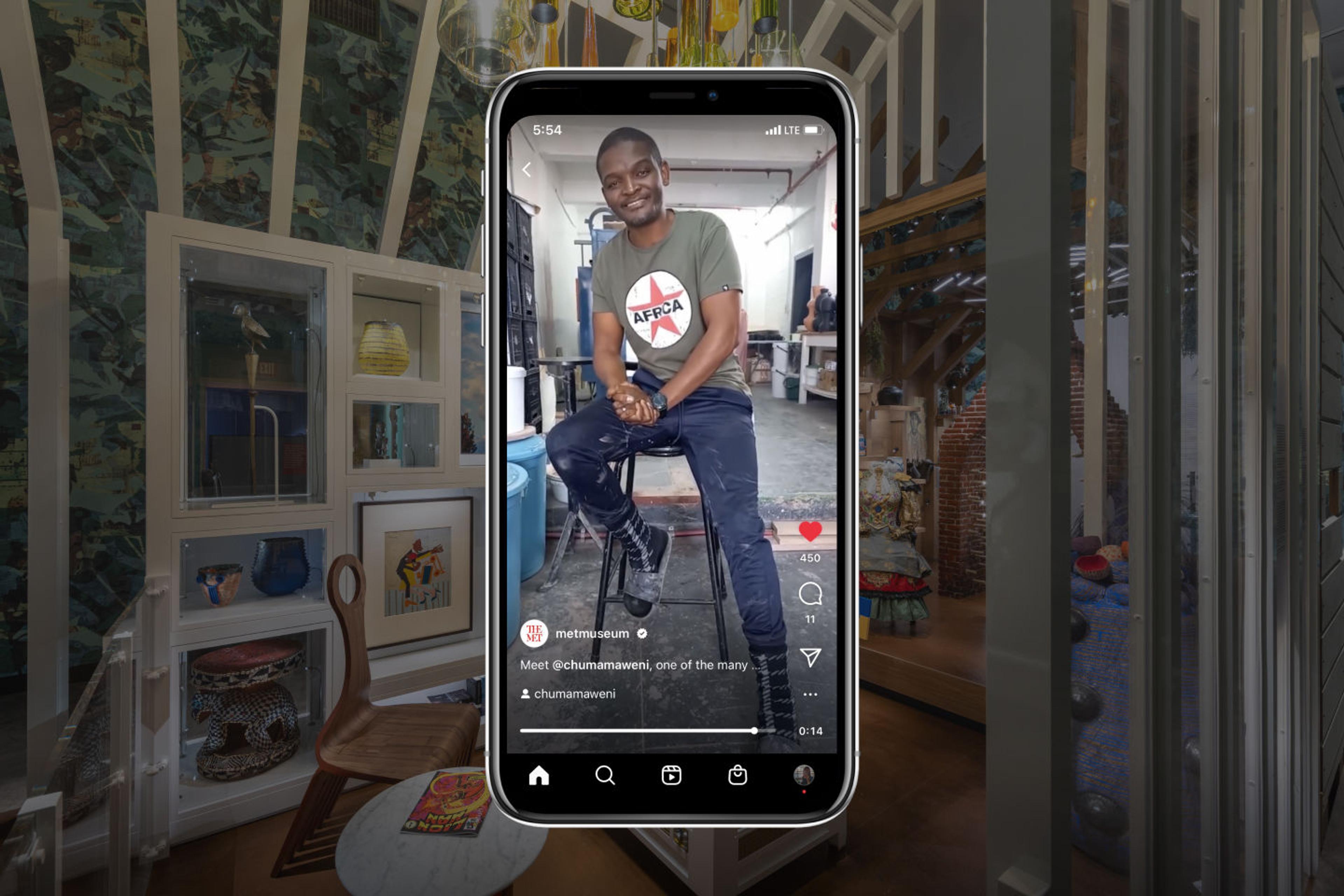 The artist Chuma Maweni sitting in a stool, the image framed in an iPhone against a blurry background of the exhibition "Before Yesterday We Could Fly: An Afrofuturist Period Room."