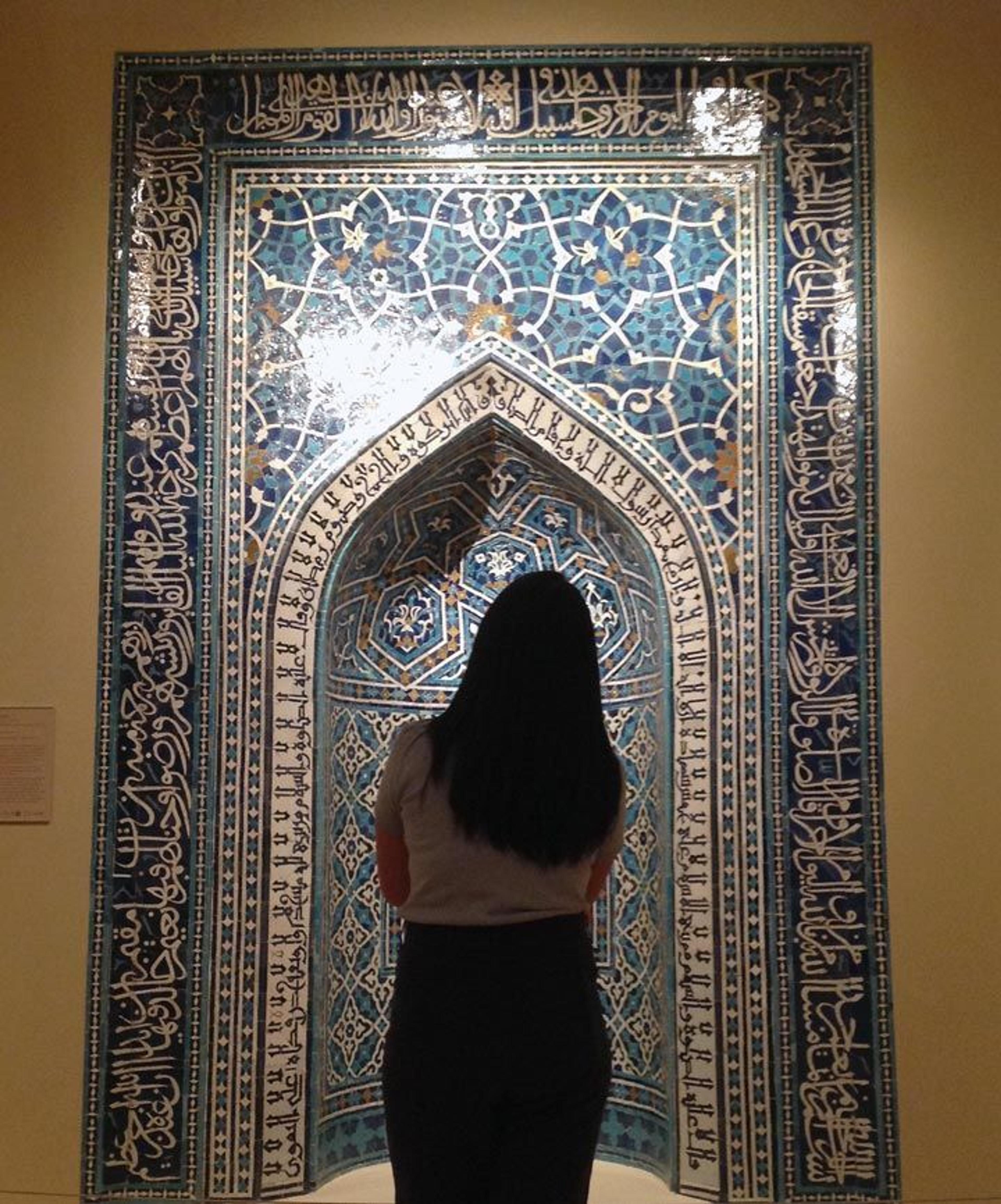 A young girl stands in front of the blue- and white-tile facade in the Islamic galleries