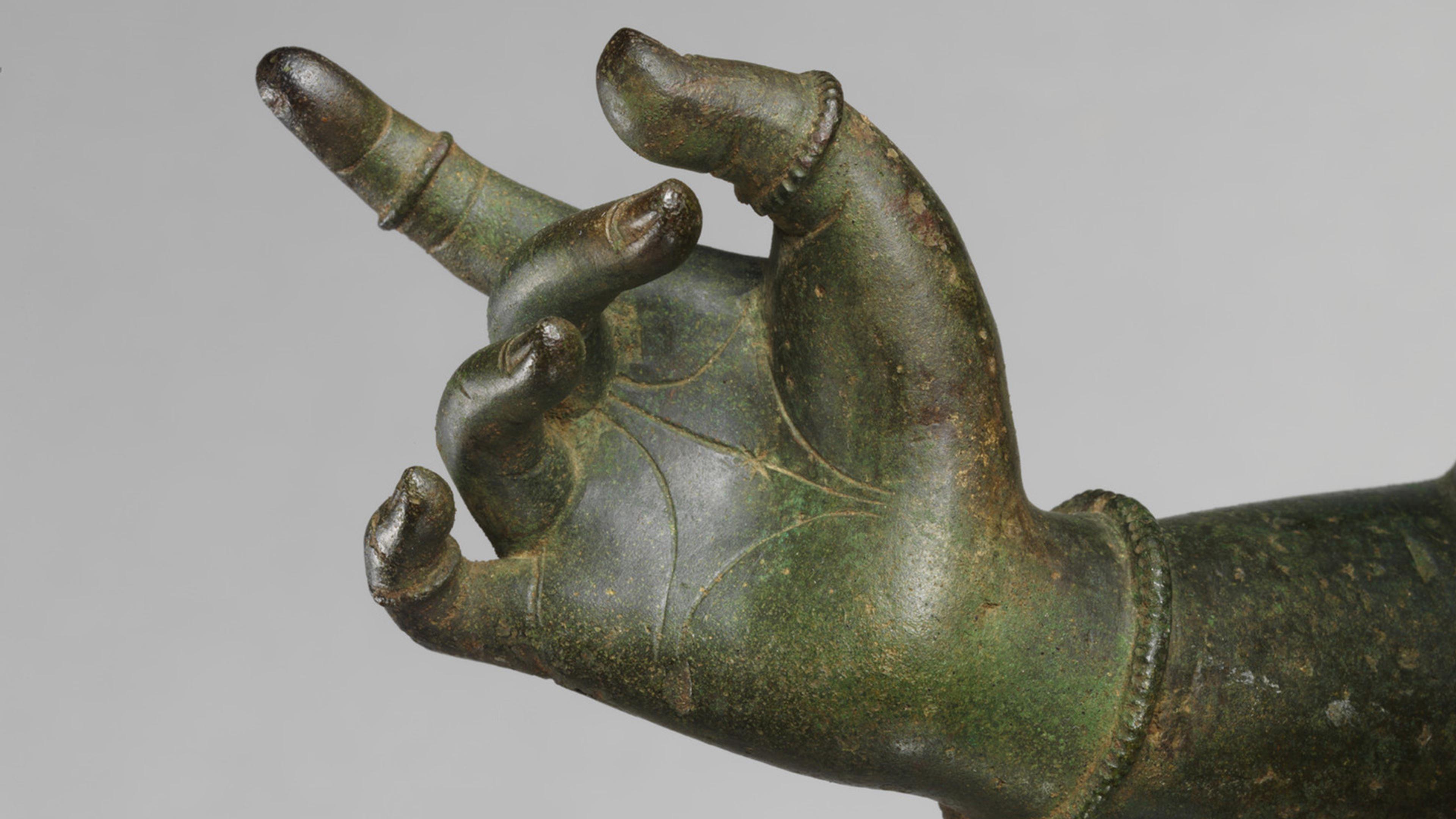 Close-up of a sculpture's right hand in a clasped position with an extended index finger.