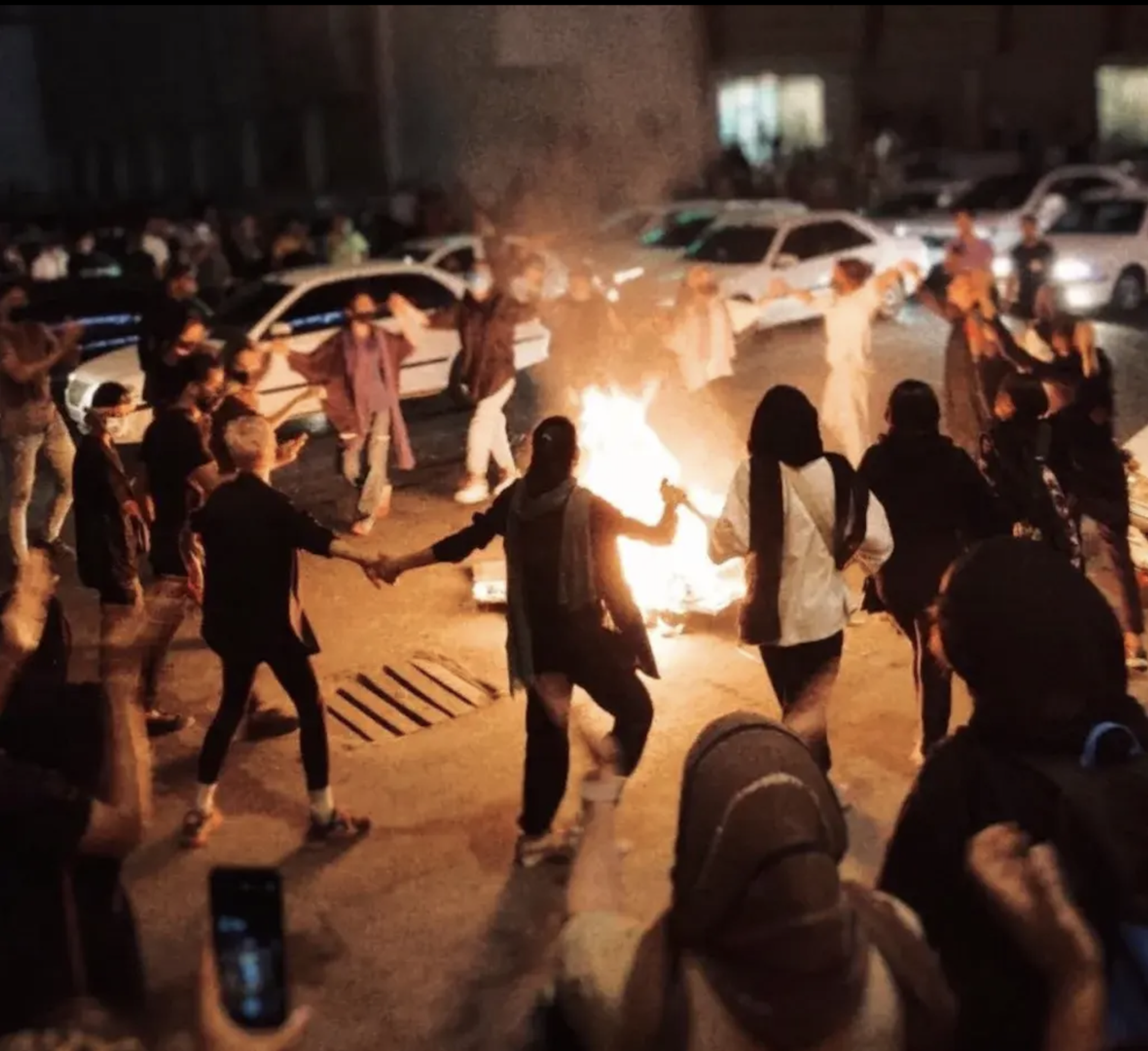 Group of women hand and hand dancing around a fire.